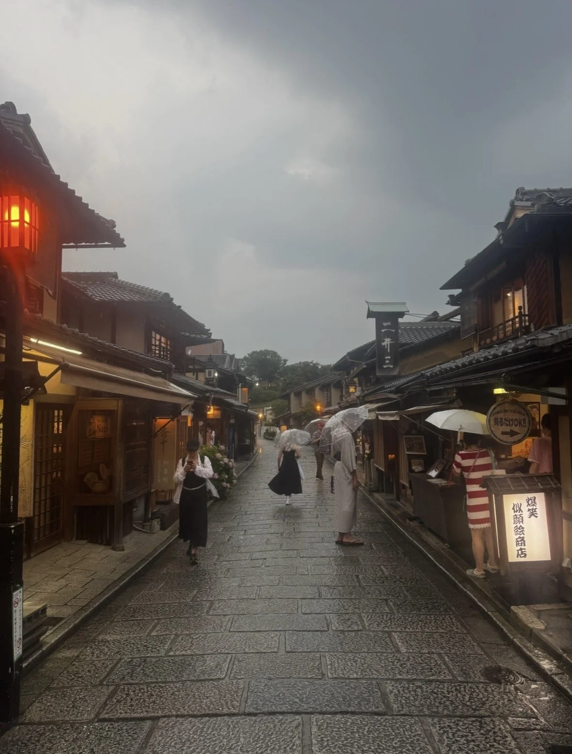 Rainy evening on a historic Higashiyama street in Kyoto with traditional wooden buildings and glowing lanterns