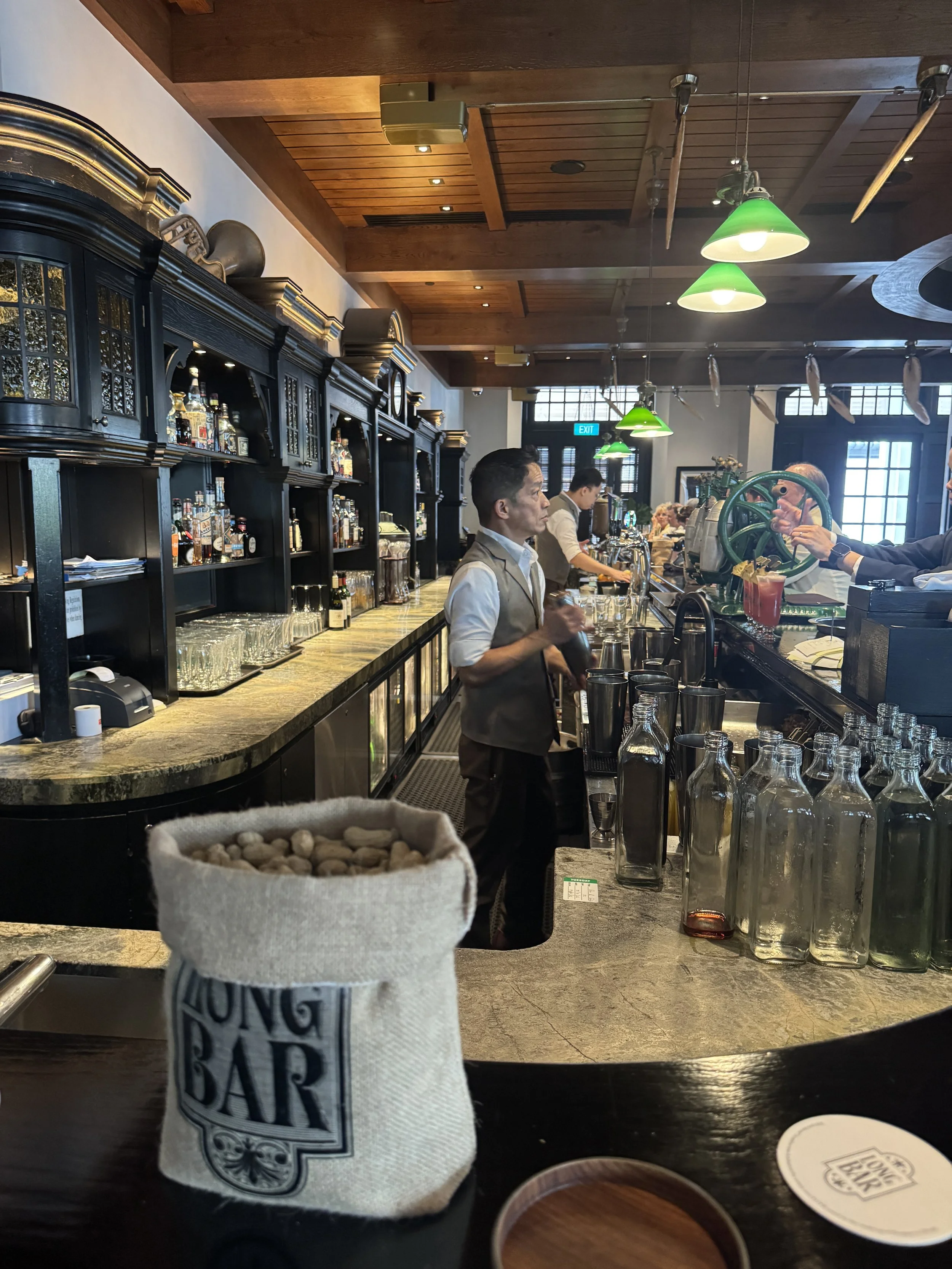 Interior of Long Bar at Raffles Singapore with colonial wood bar and green hanging lamps