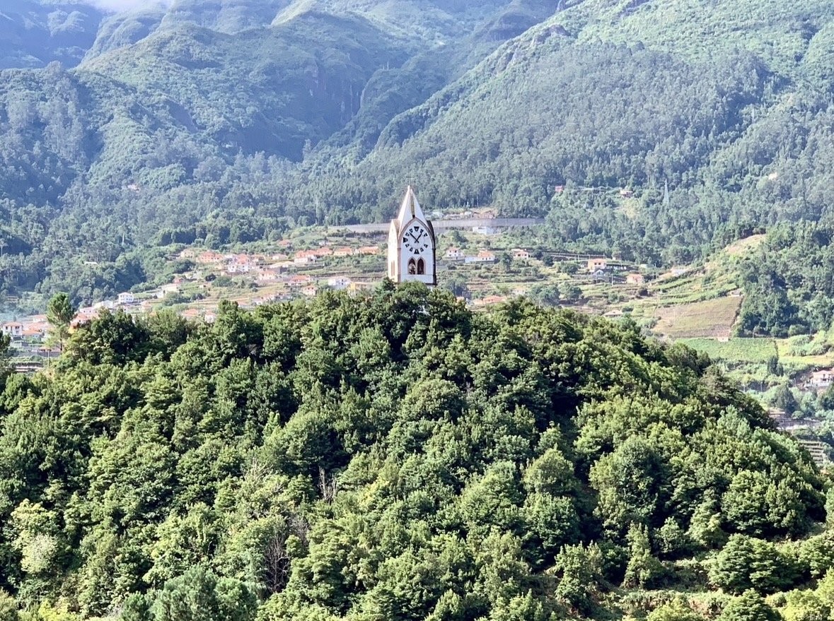 Panoramic view of a church surrounded by lush green mountains in Madeira, Portugal.