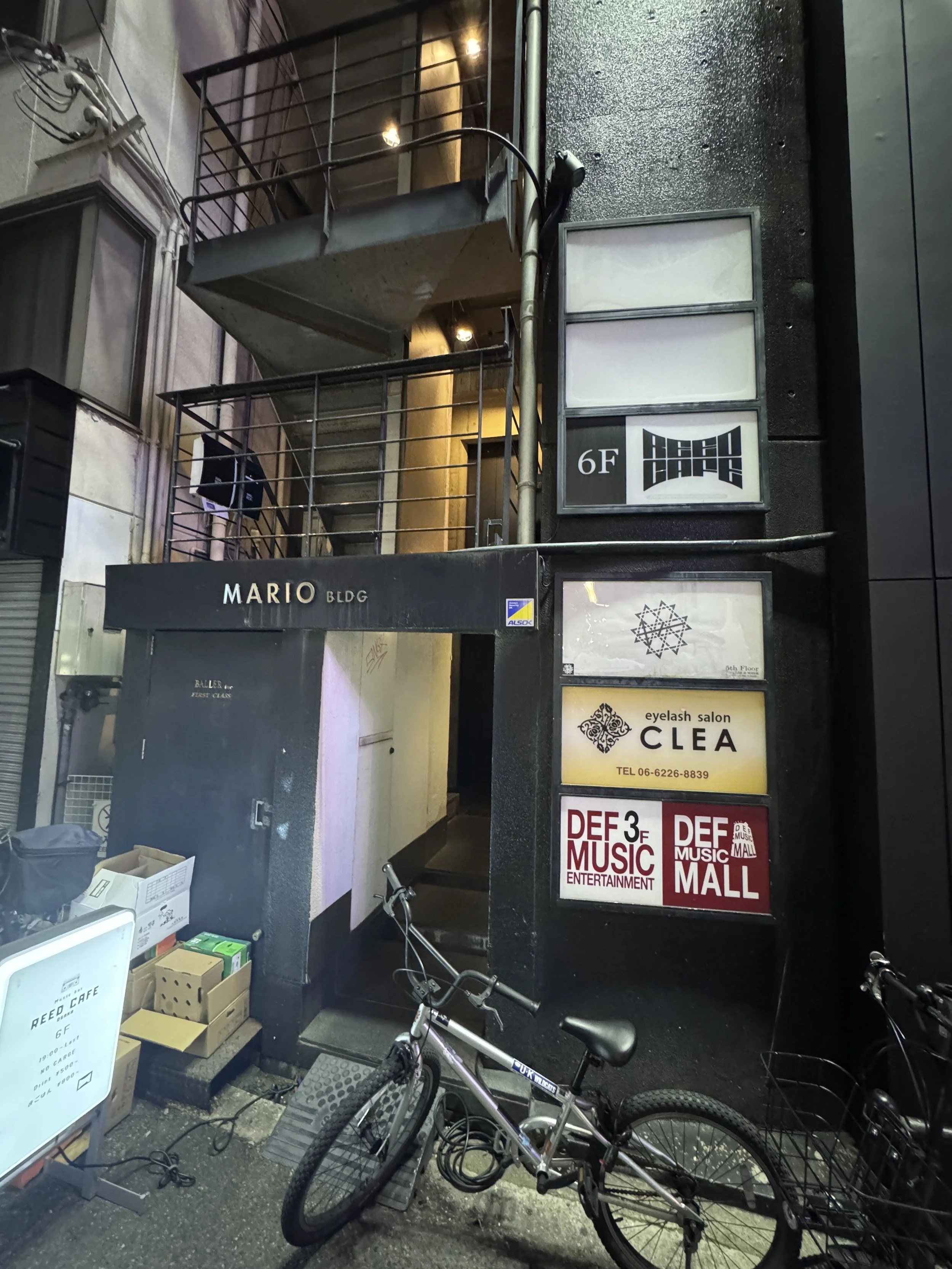 Photo of the entrance to a multi-story building with signs for various businesses, including an eyelash salon and a music entertainment store, with bicycles parked outside on the sidewalk.