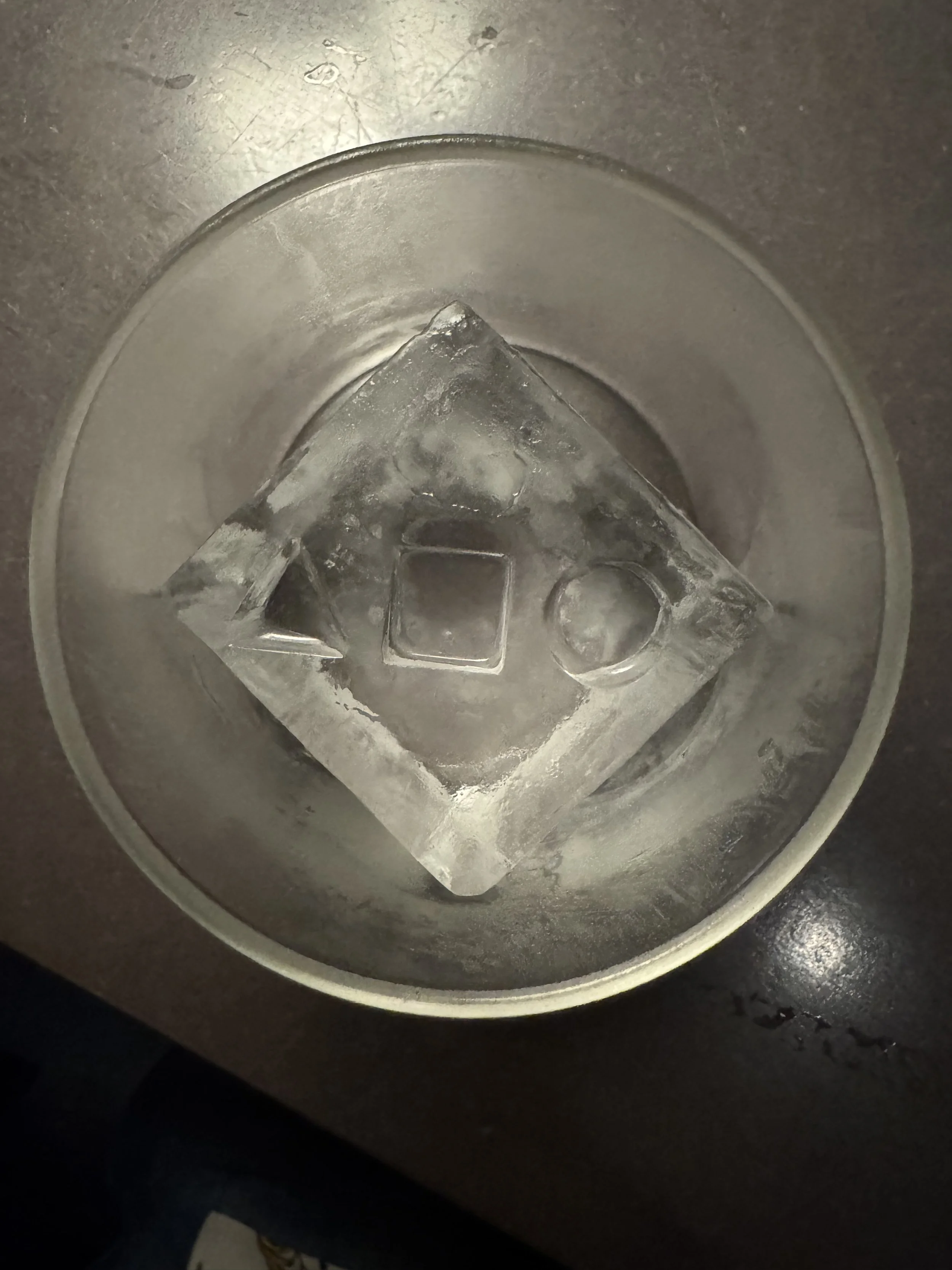 Close-up image of a circular metal container with a clear ice cube inside.