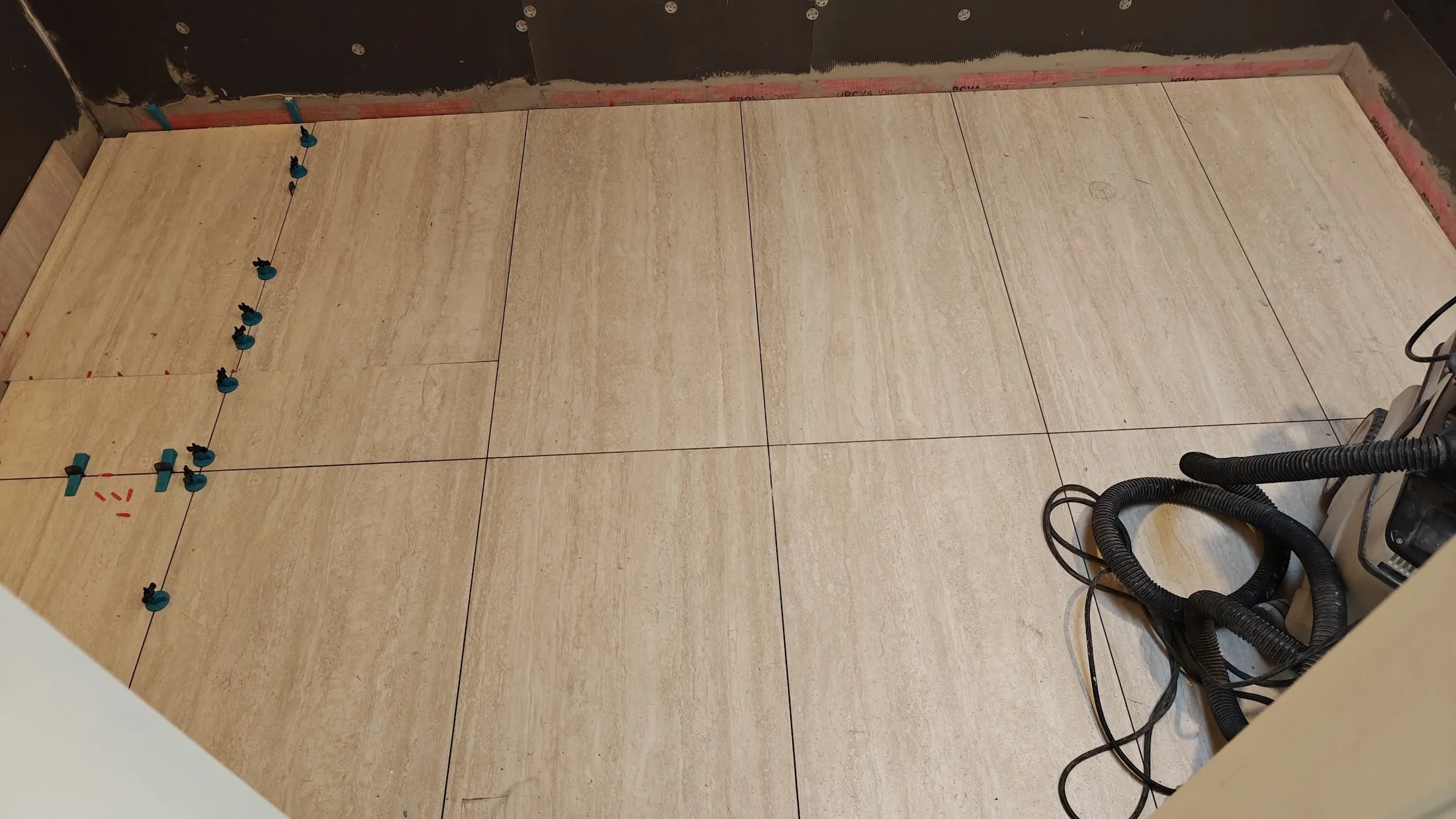 Tile flooring with construction tools and hoses, near a partially painted wall in a room under renovation.