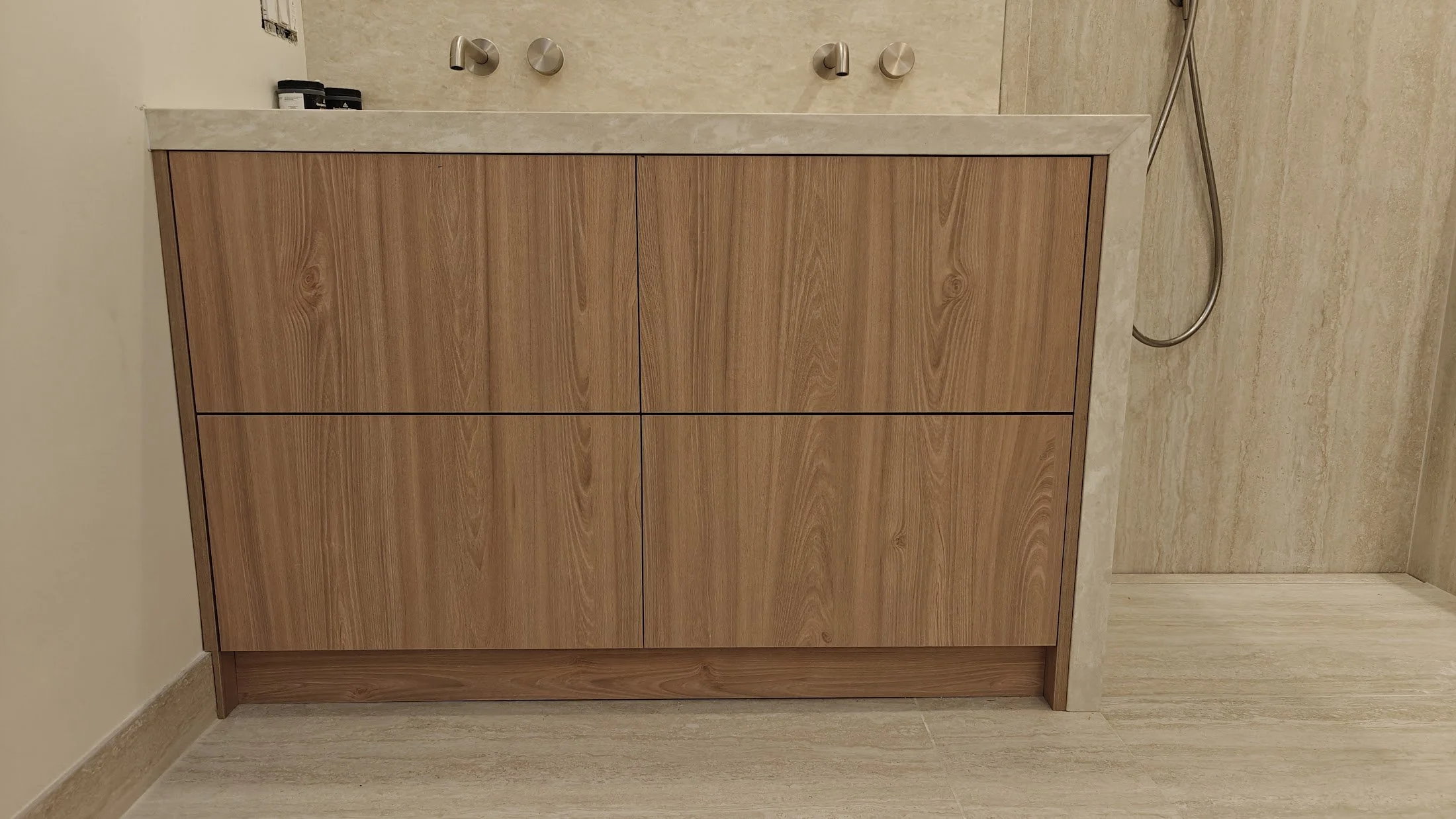 Bathroom vanity with wooden cabinet, beige countertop, wall-mounted faucet, and shower hose on the right side.