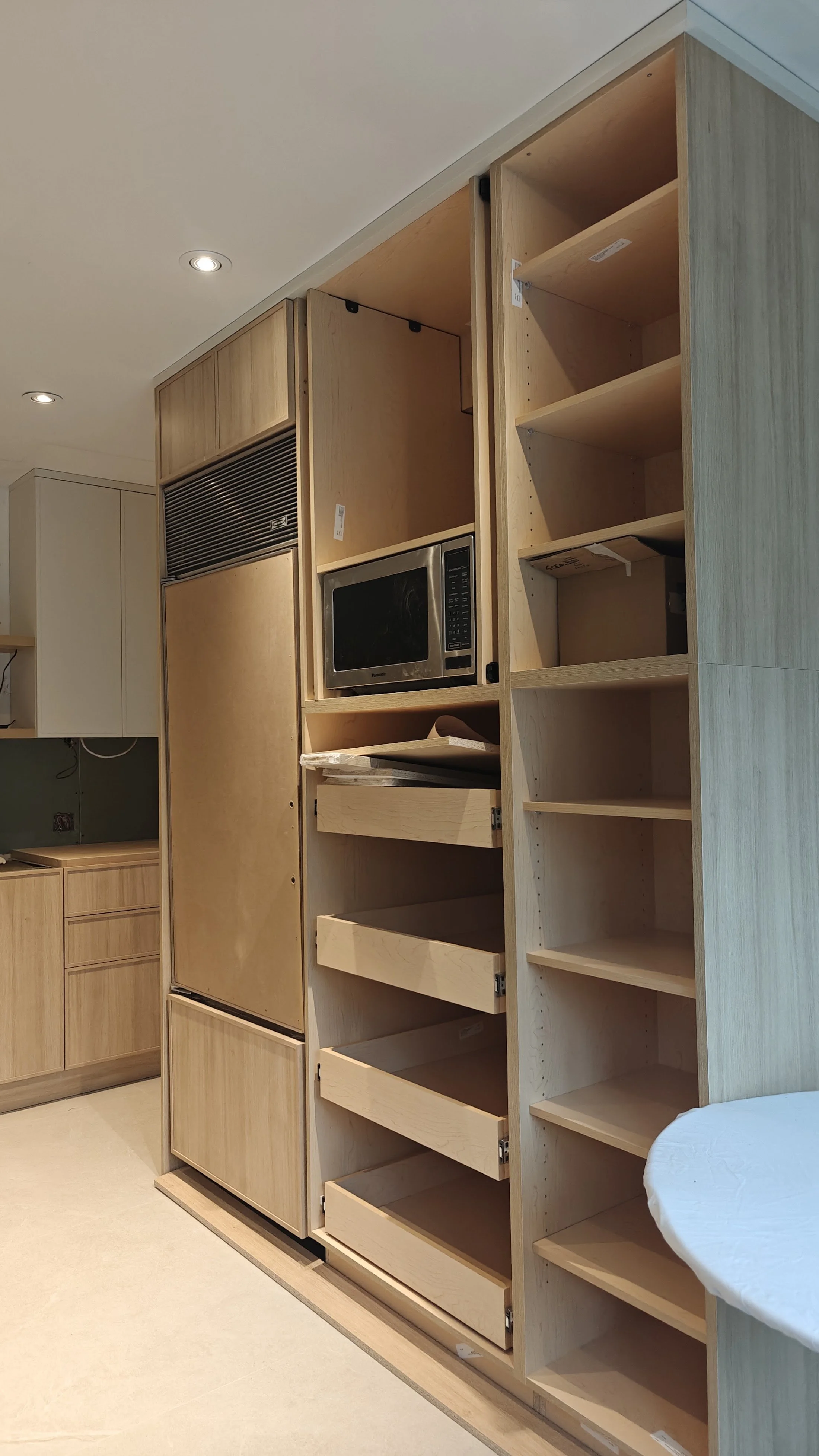Unfinished wooden kitchen cabinets and shelves with drawers, a microwave, and a vent hood, in a home renovation setting.