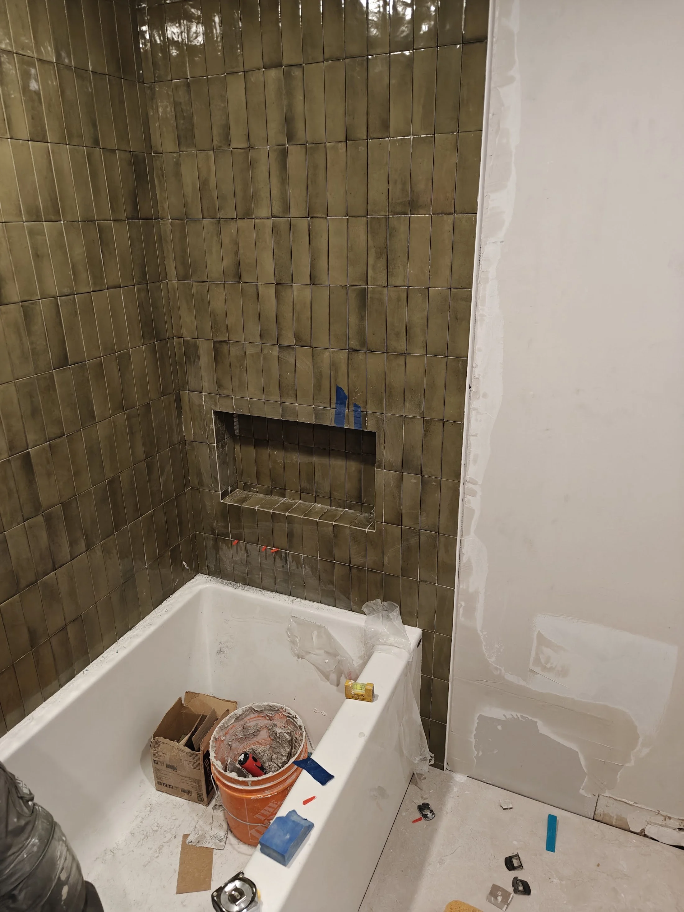 Bathroom renovation in progress with brown tiled wall, partially painted white wall, construction tools, and materials scattered around.