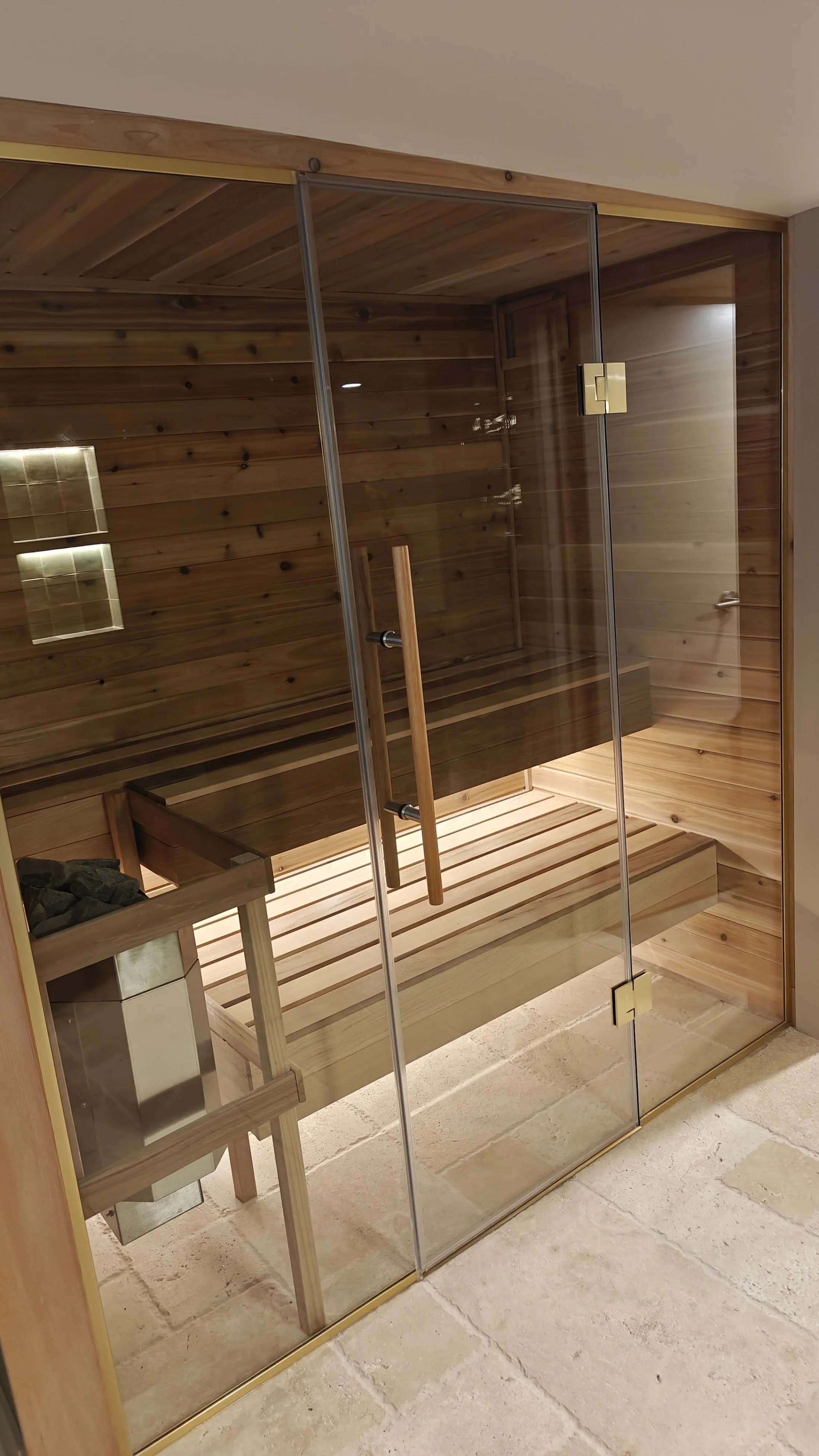 Inside a wooden sauna with a glass door, wooden bench, and heater with stones.