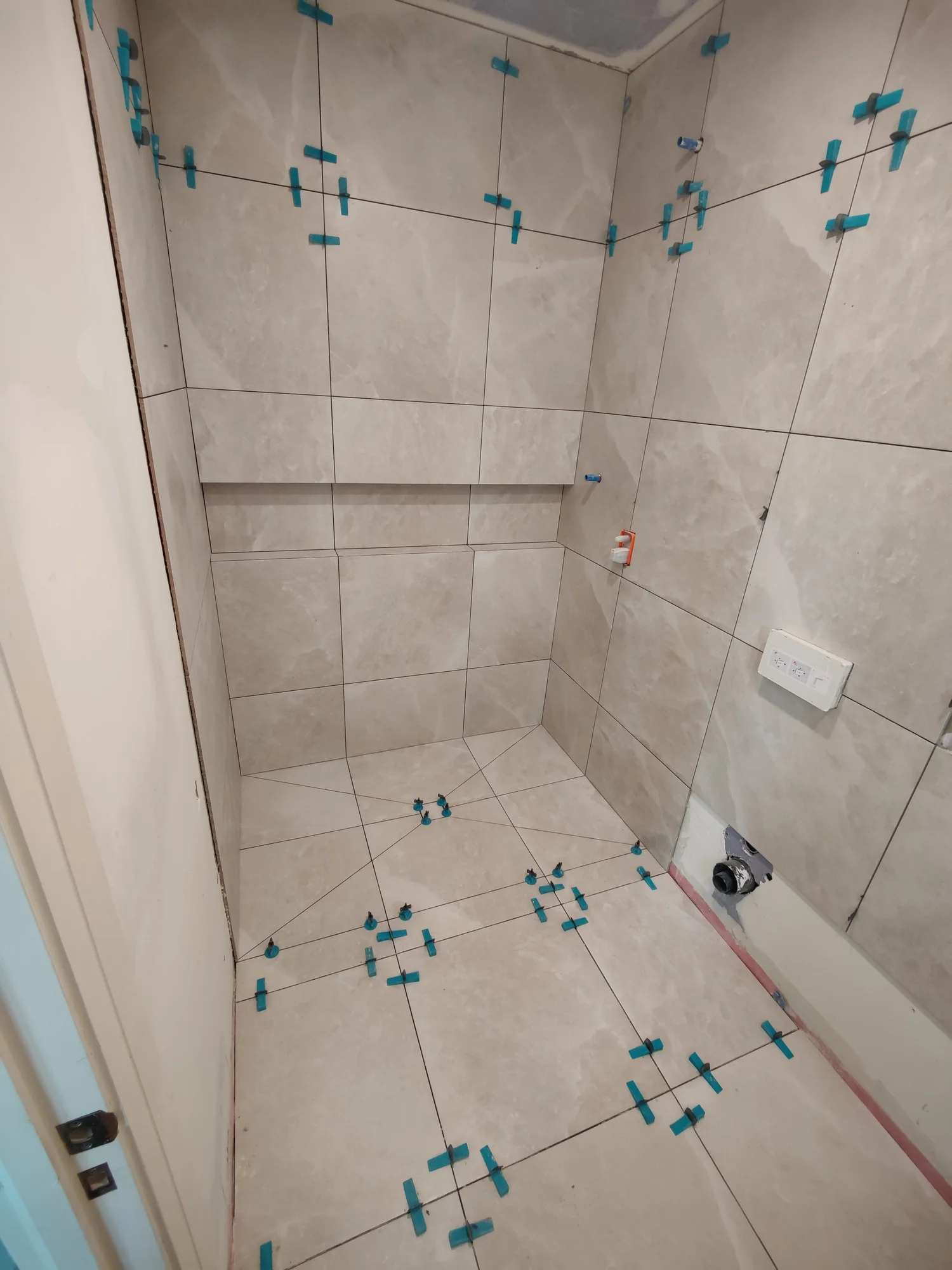Shower walls and floor tiled, with leveling clips still in place