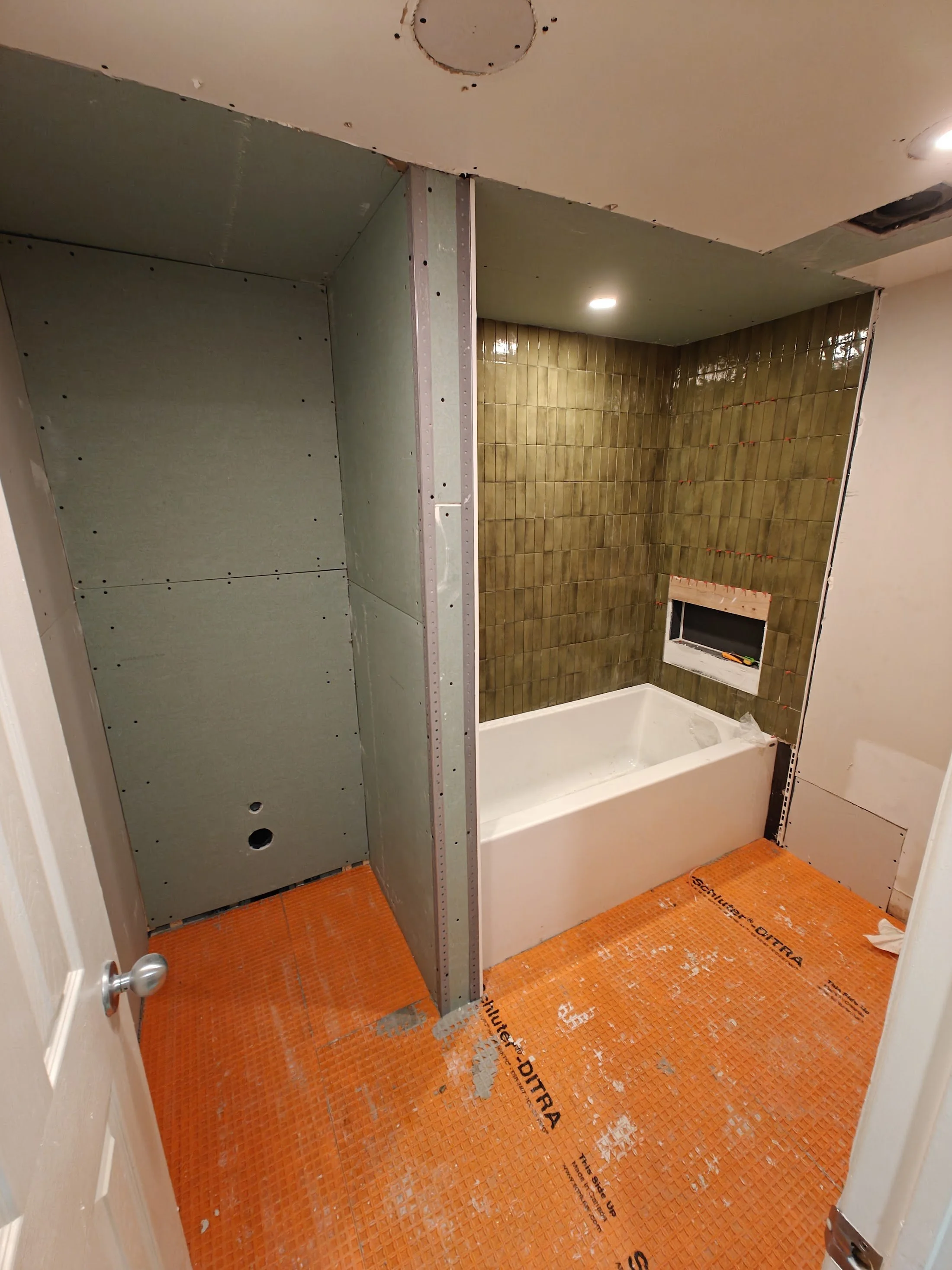 Bathroom under renovation with partial drywall installation, a bathtub, and orange waterproofing membrane on the floor.