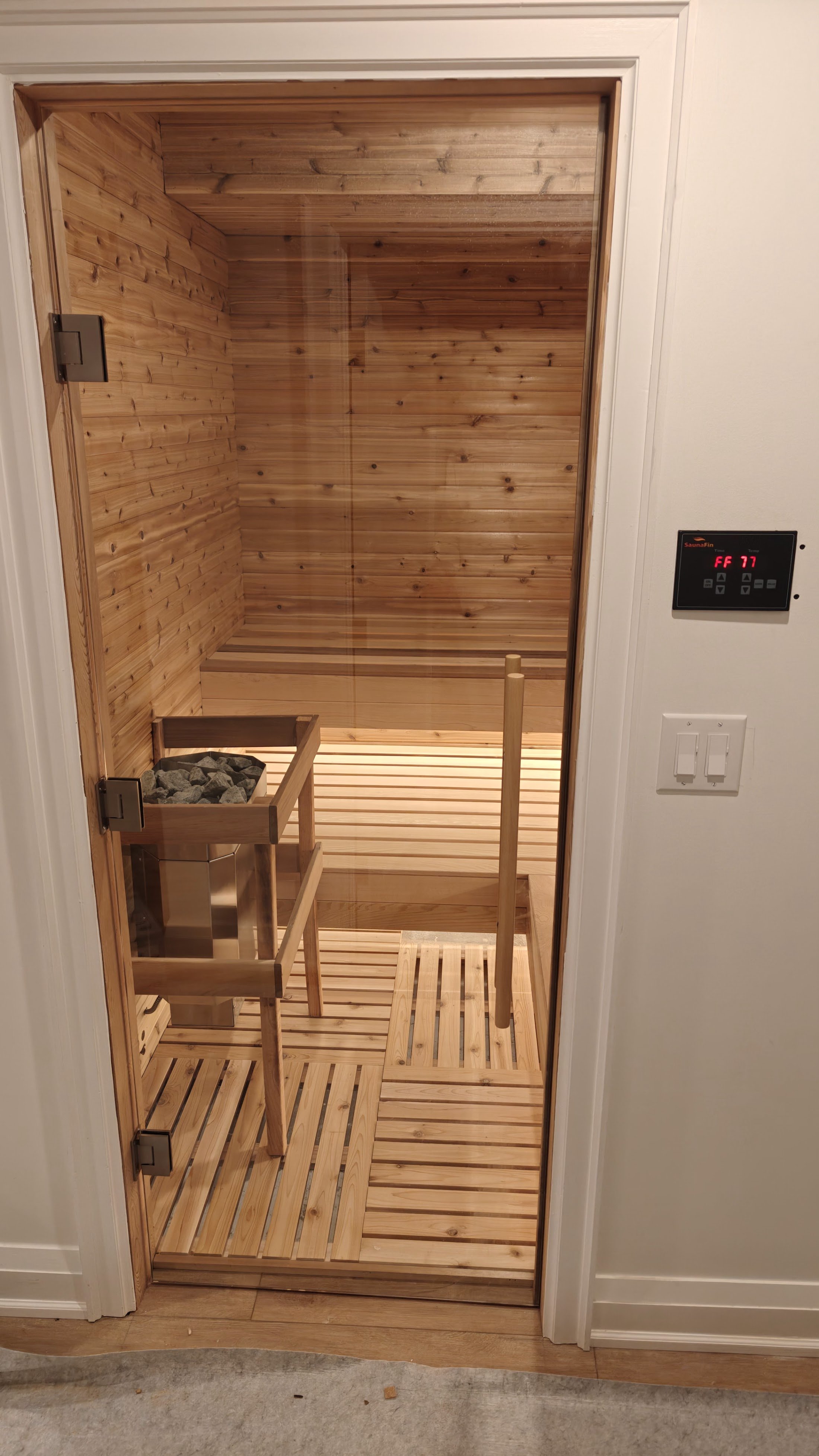 A small, enclosed wooden sauna with benches and a heater filled with rocks.