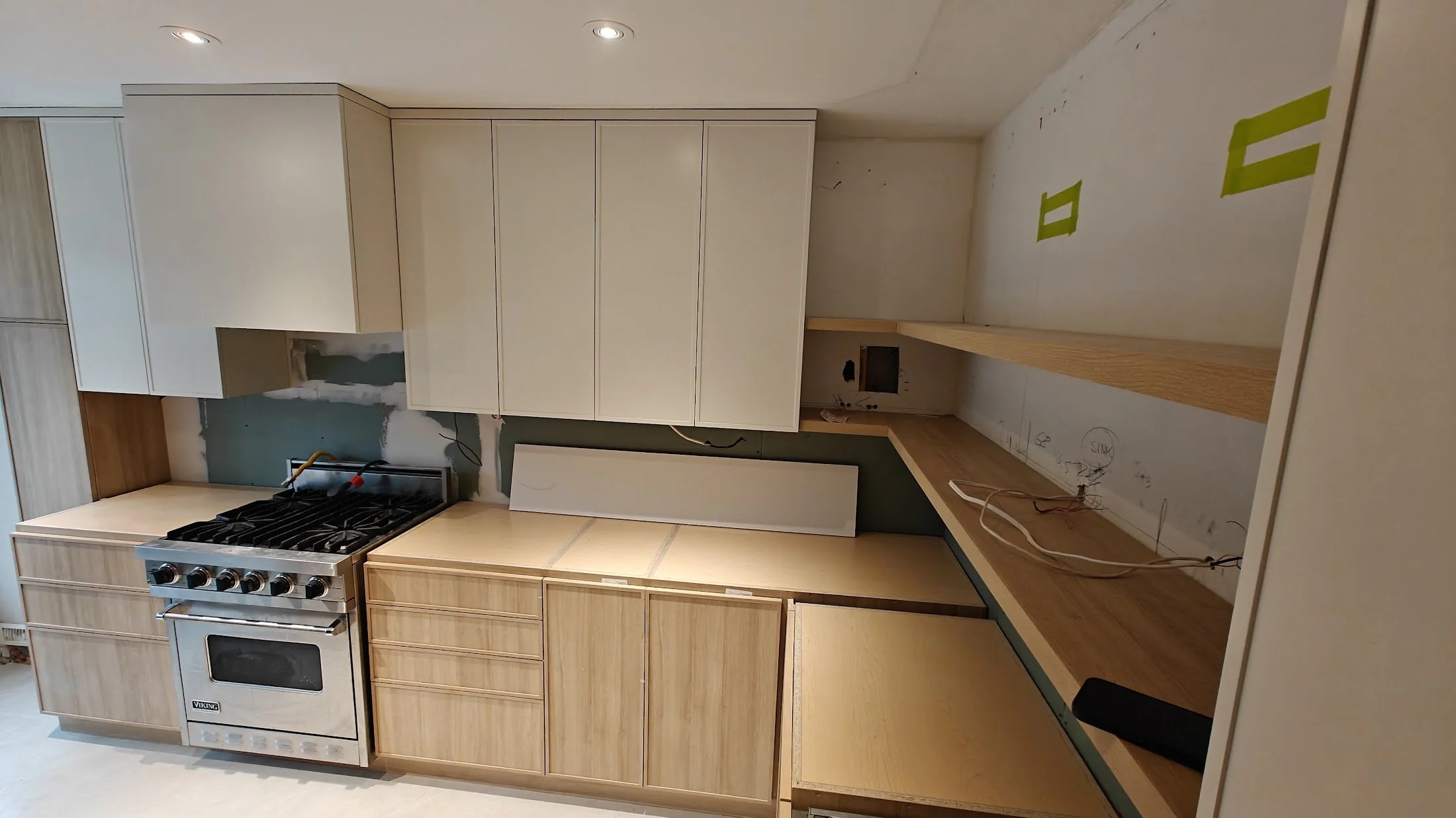 Unfinished kitchen with wooden cabinets, a stove, an empty countertop, and construction wires.