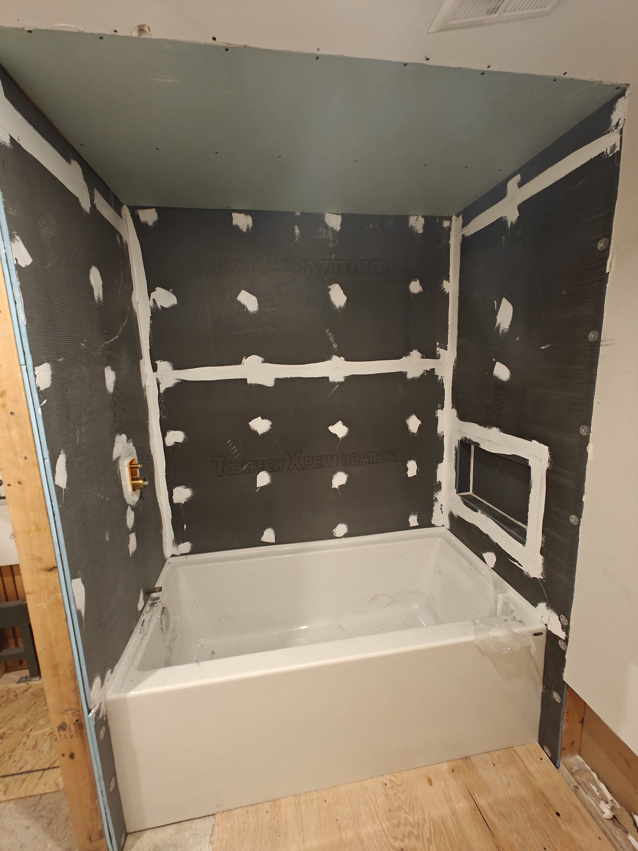 Bathroom with drywall and water-resistant backer board installed around a bathtub, with drywall screws visible, and the bathtub is unfinished.