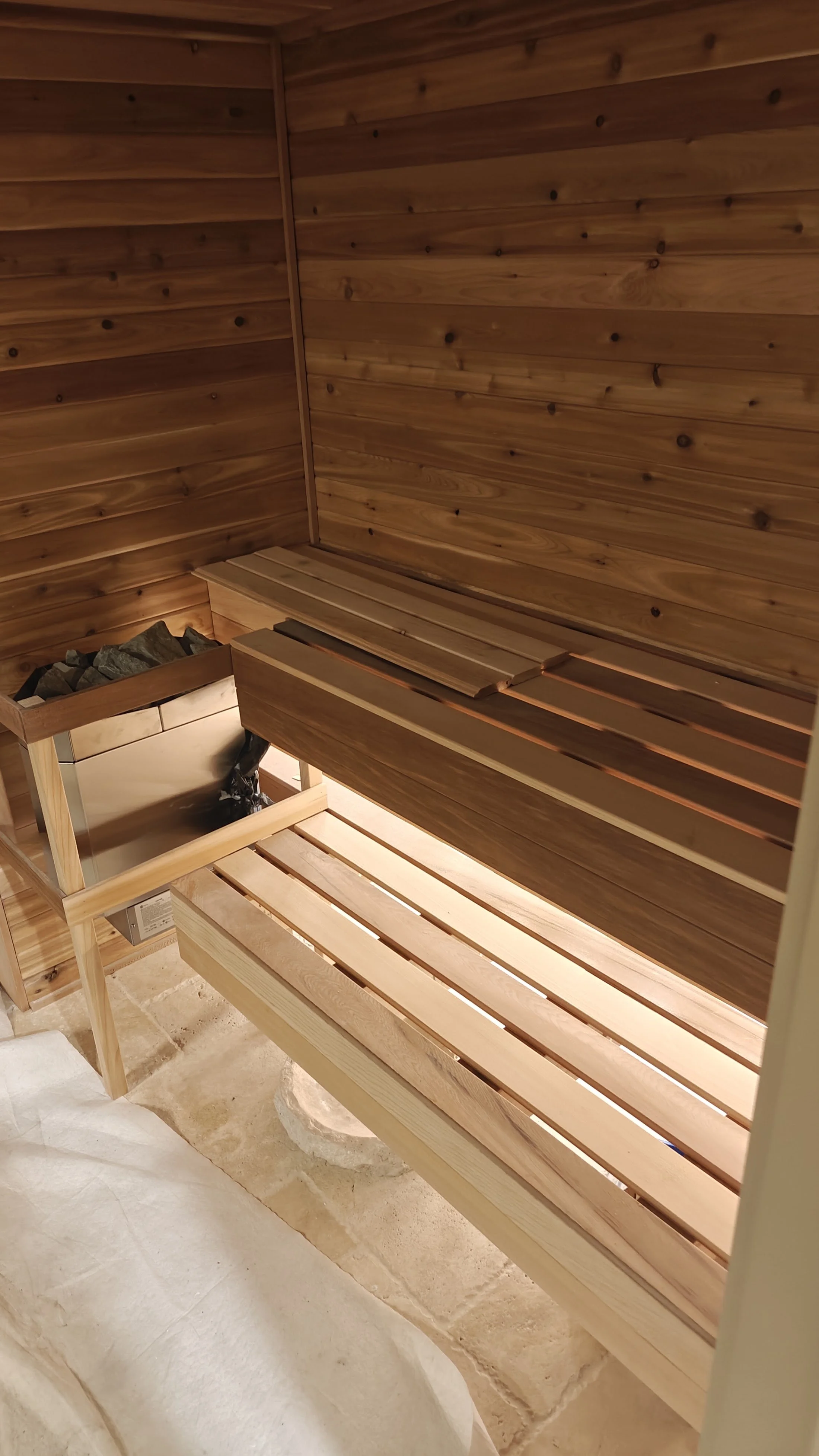 Interior of a traditional sauna with wooden walls, benches, and a heater with rocks.