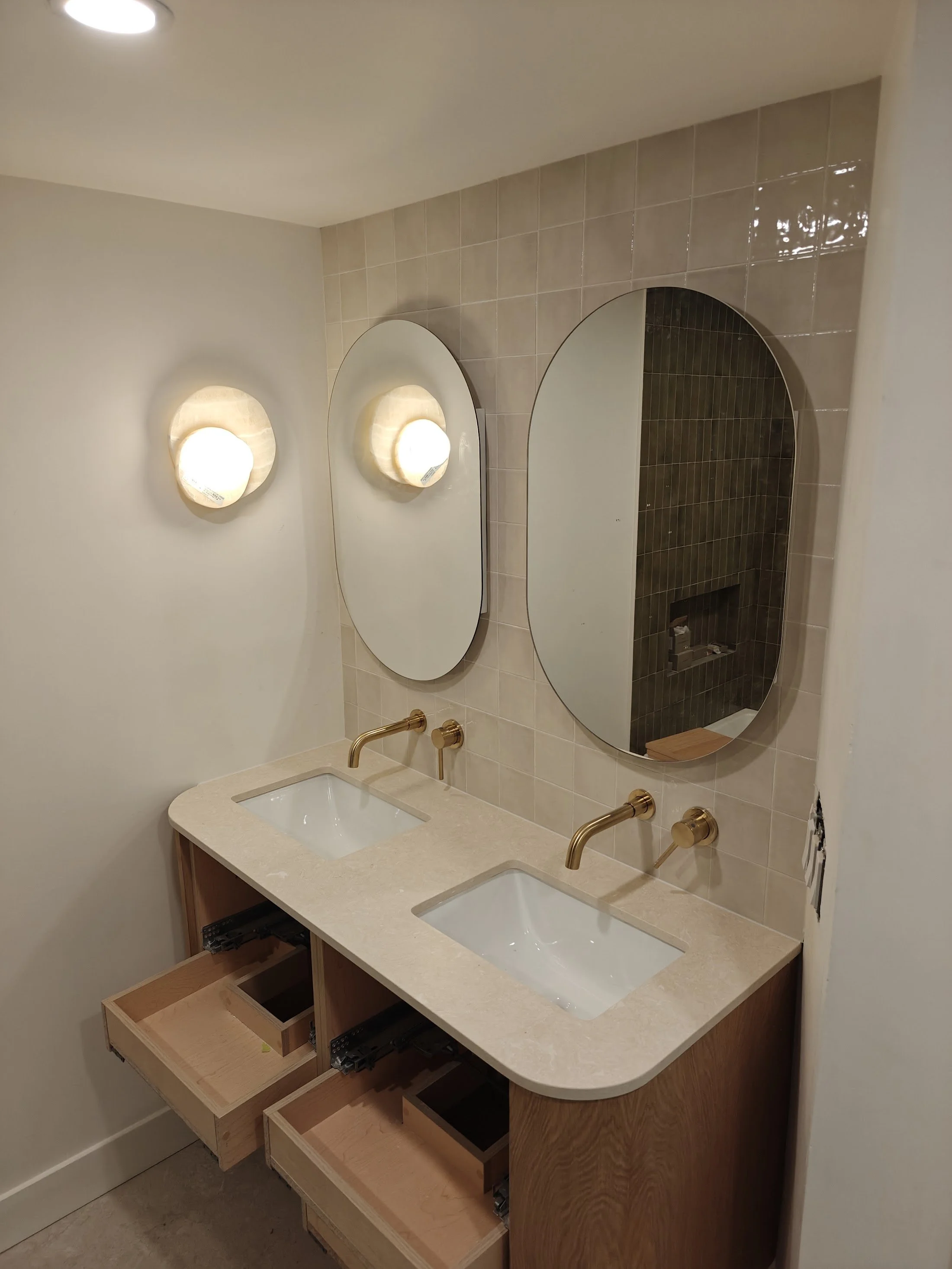 Bathroom vanity with two sinks, three open drawers, and two large mirrors, with wall-mounted lights and brass fixtures.