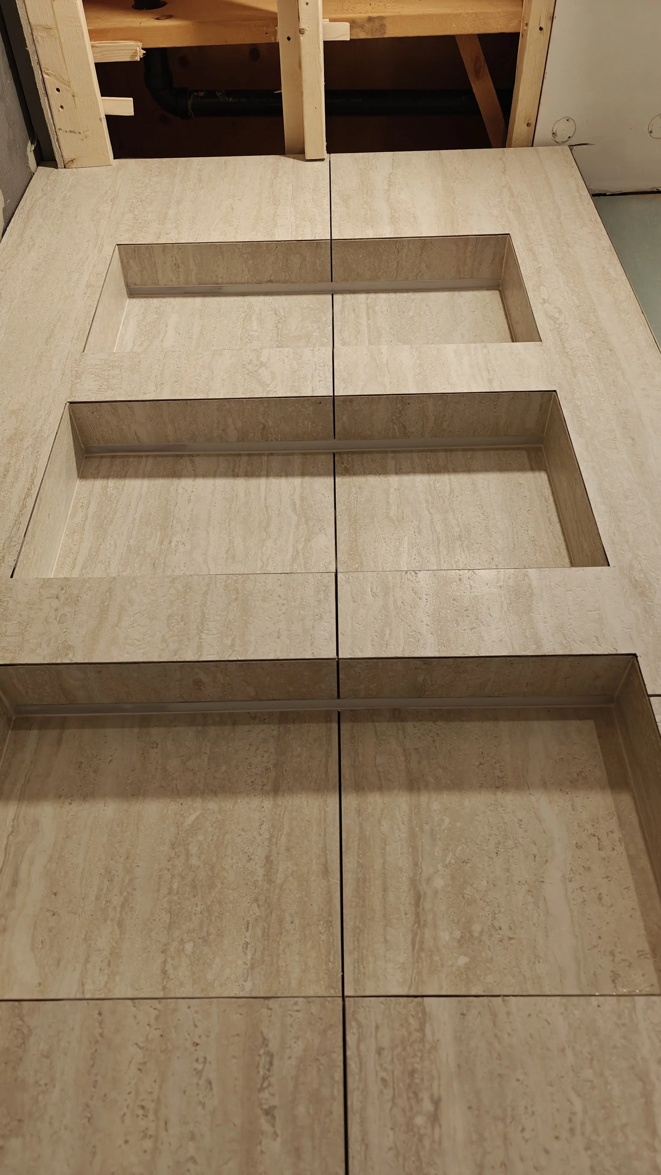A close-up view of beige stone tiles with three rectangular cutouts in a row, part of a construction or renovation project.