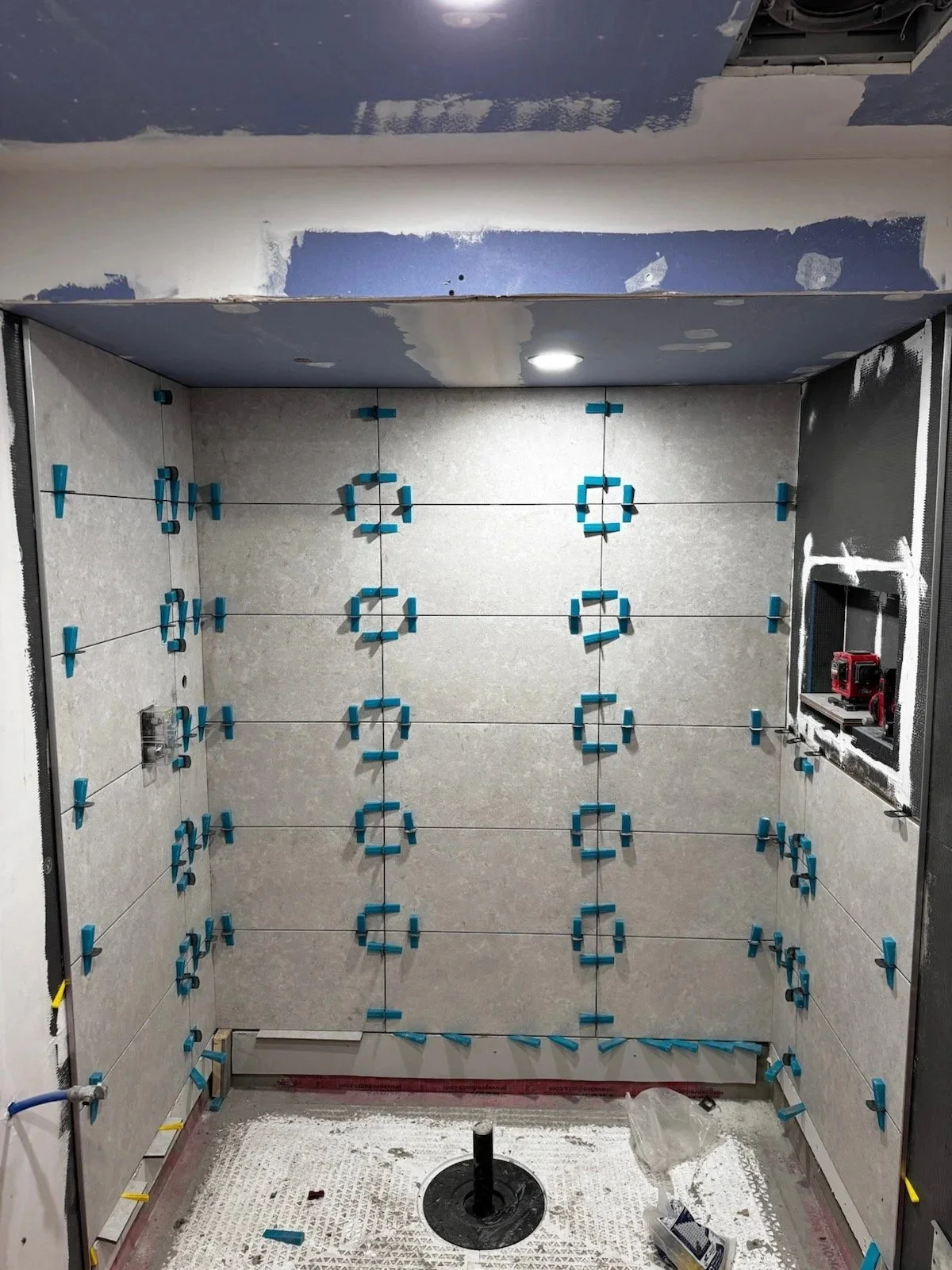 Shower walls tiled with leveling clips at every joint, a niche on the side wall and the floor drain ready for tile, in a Toronto bathroom