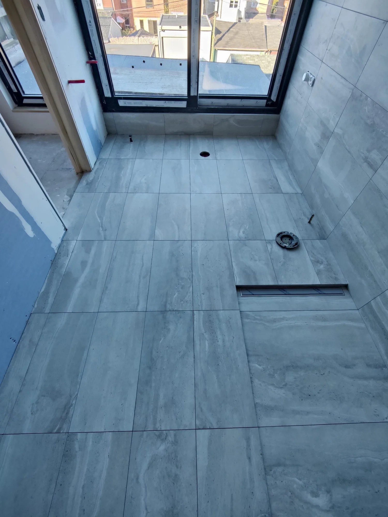 Finished bathroom floor in long stone-look tile with a linear drain near the window, in a Toronto home