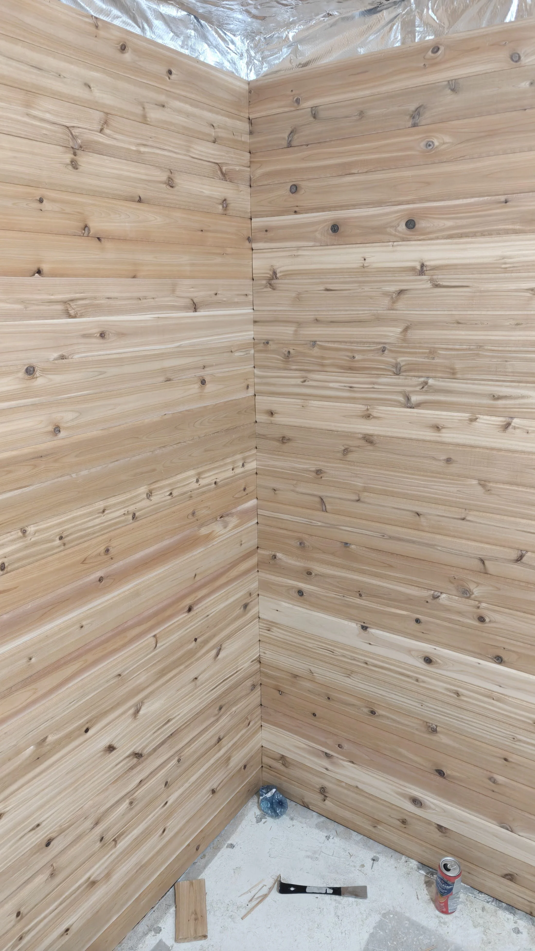 Interior corner of a wooden room with horizontal wooden paneling on the walls, construction tools and supplies on the floor.