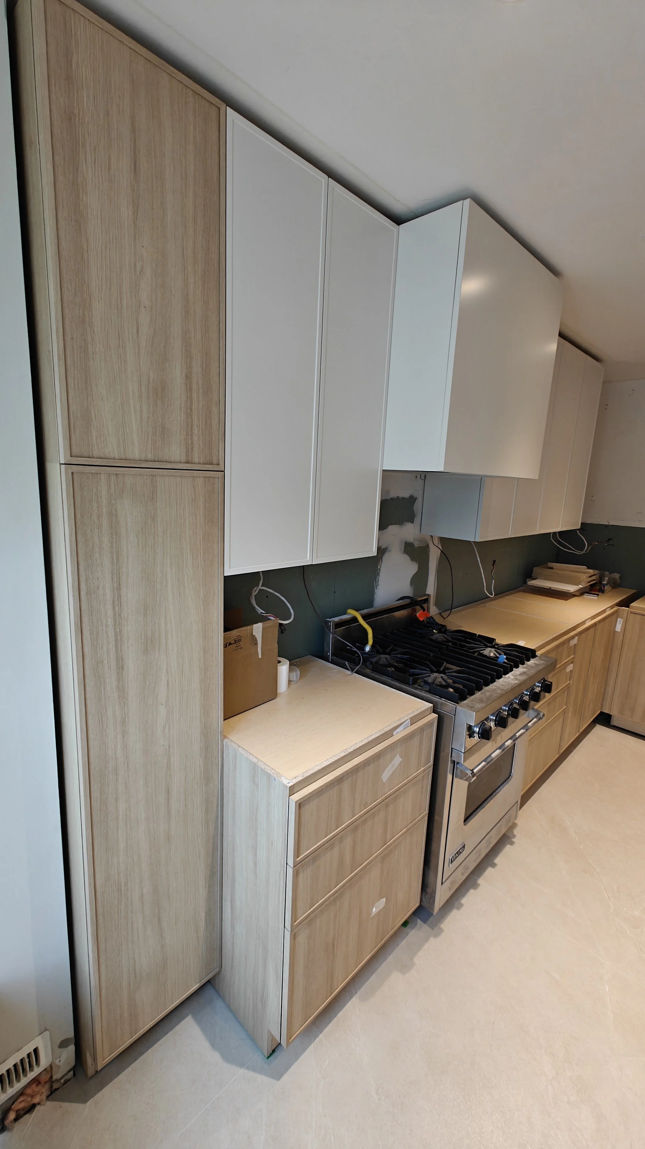A kitchen under construction with wooden and white cabinets, a stove, and unfinished walls.