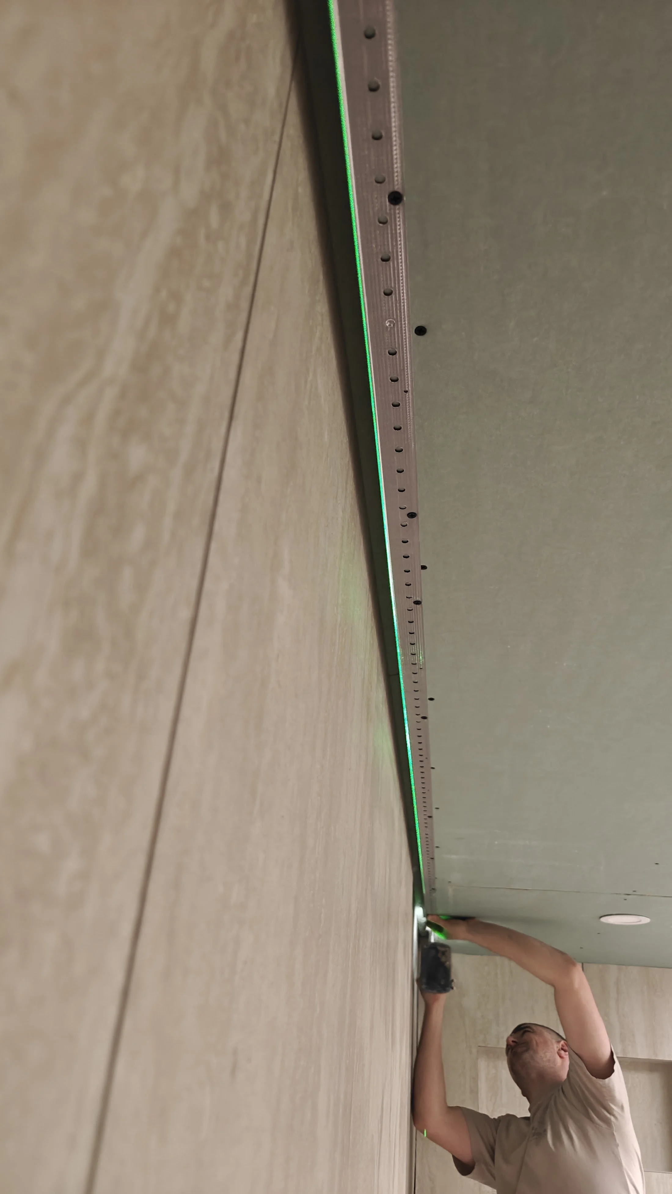 A person kneeling on the floor installing or inspecting a ceiling LED strip light, with a focus on the ceiling and the person's upper body.
