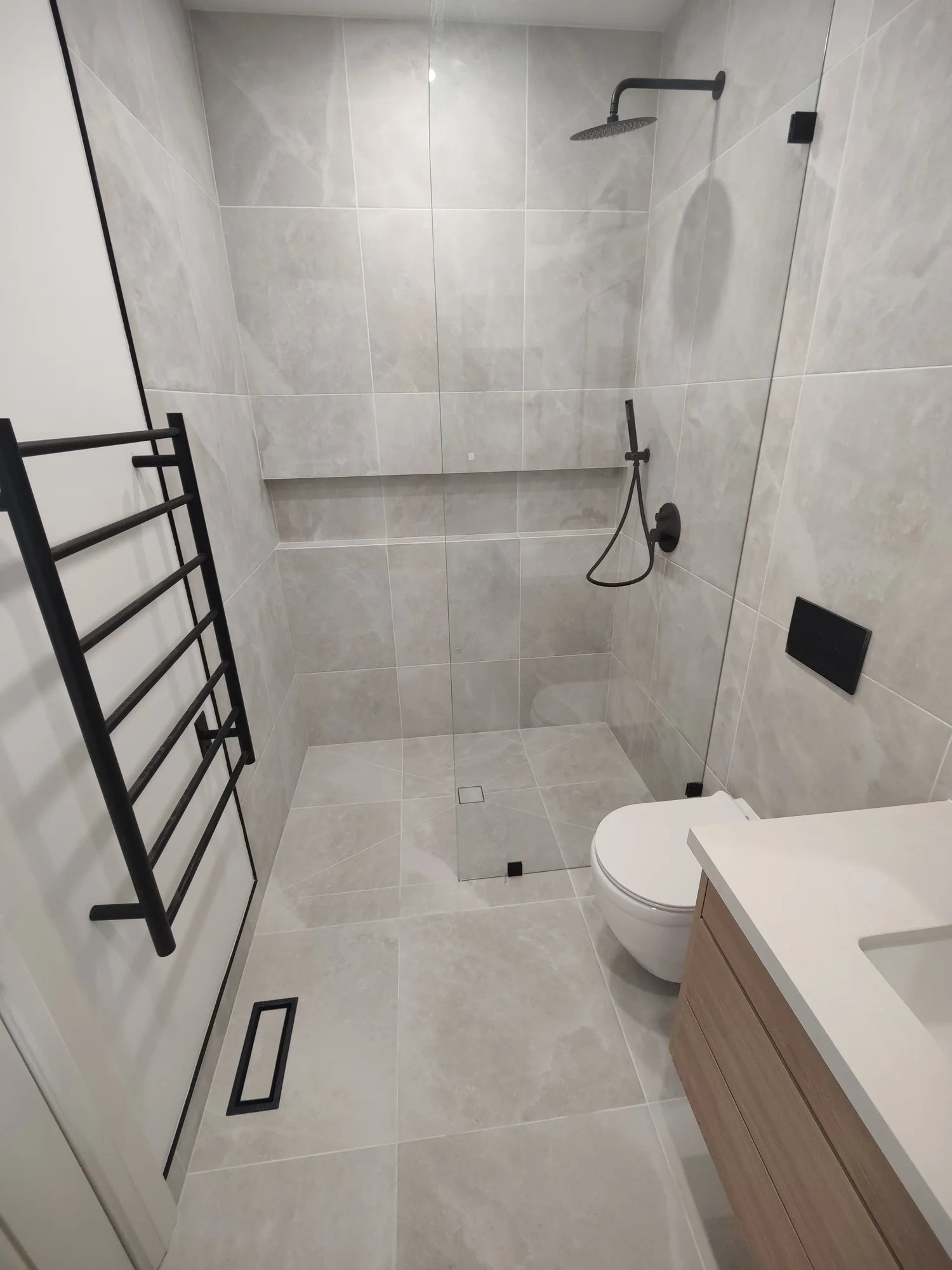 Finished curbless ensuite with continuous floor tile, a frameless glass panel and a wall-hung toilet