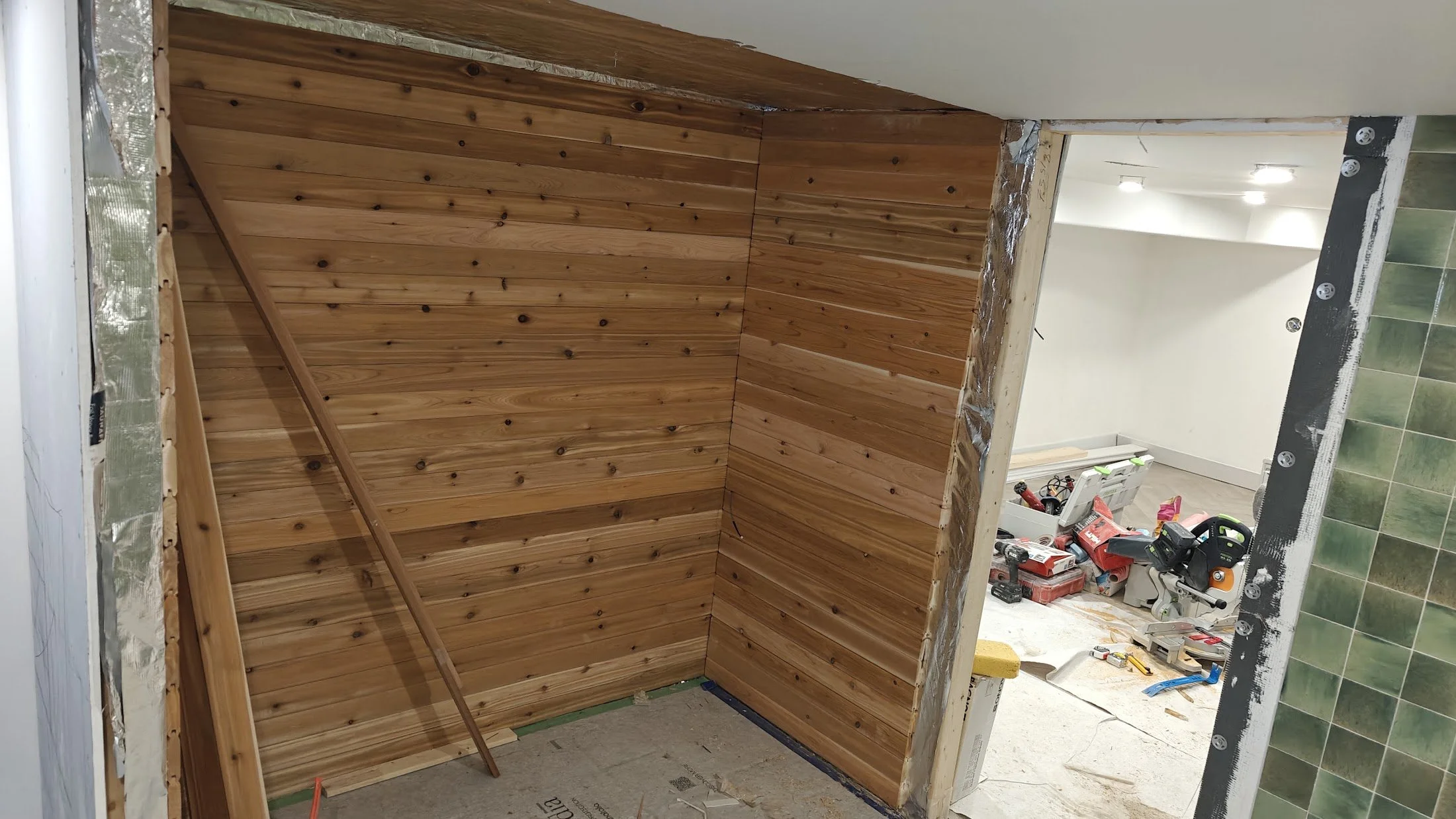 This image shows a room under construction with wooden paneling on the walls, construction tools, and materials scattered around, indicating ongoing renovation work.
