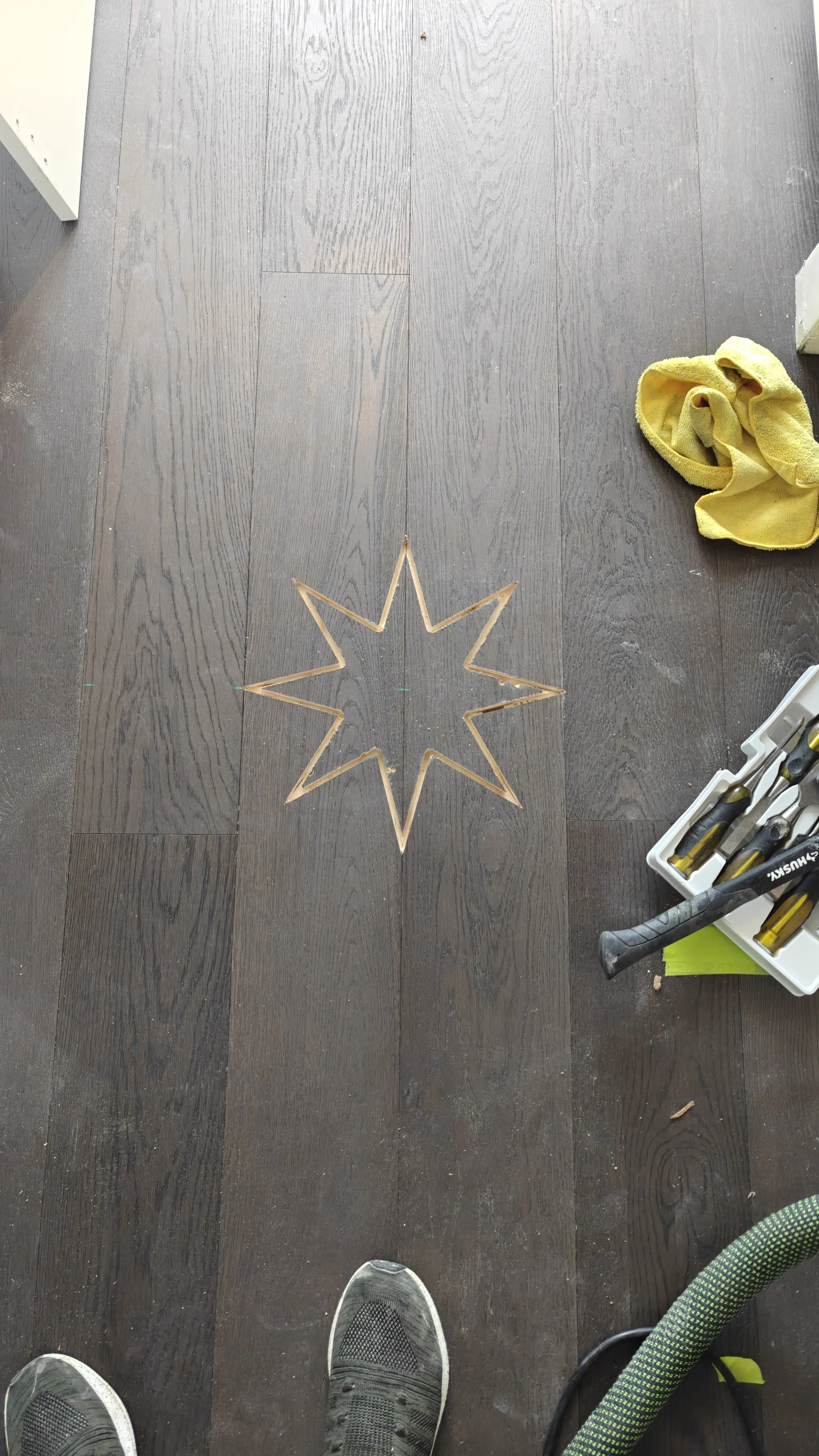 Star-shaped inlay outline marked on dark wood flooring during installation.