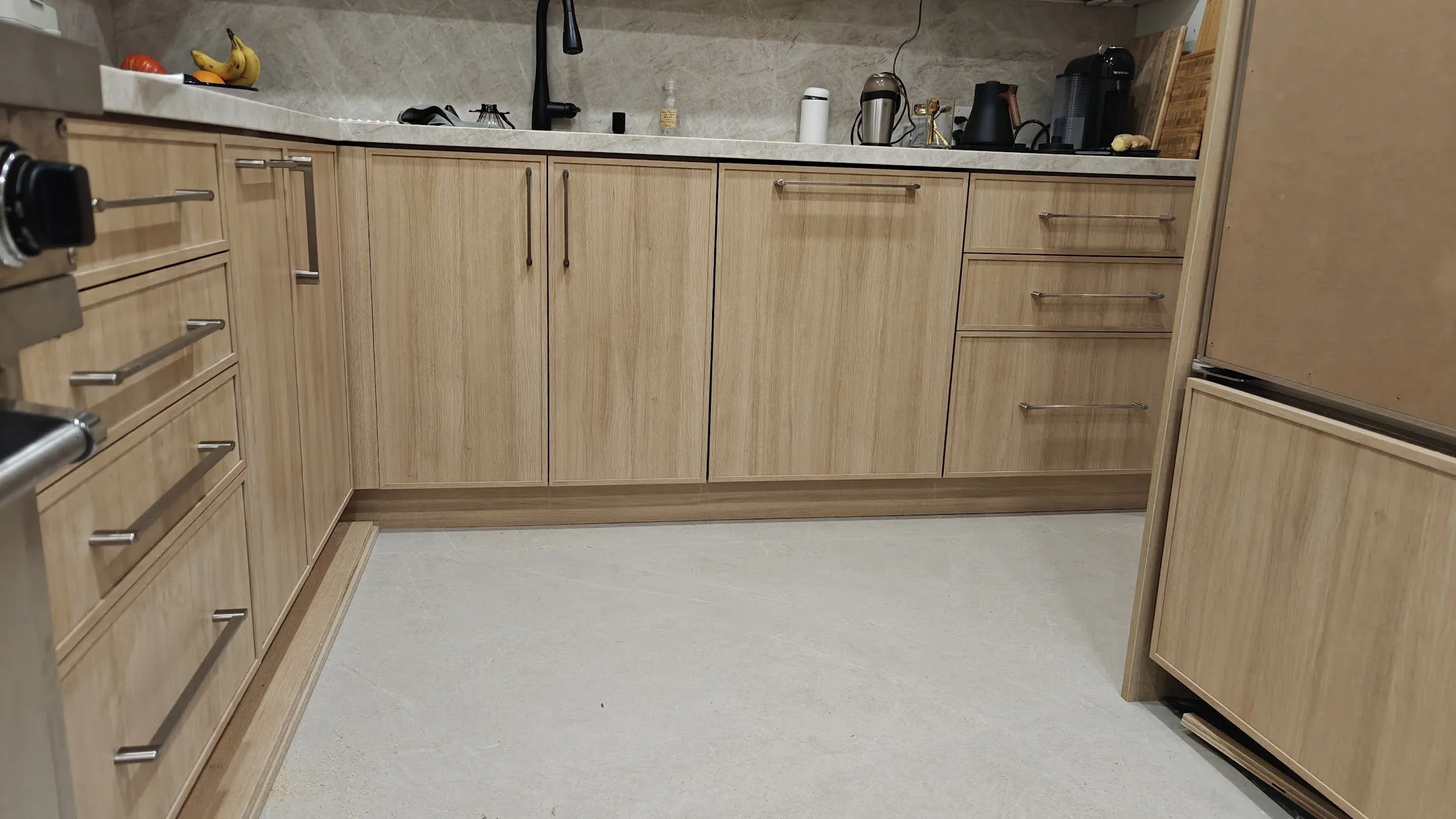 Wooden kitchen cabinets with a light finish, a beige countertop, and various appliances including a blender, coffee maker, and thermos.