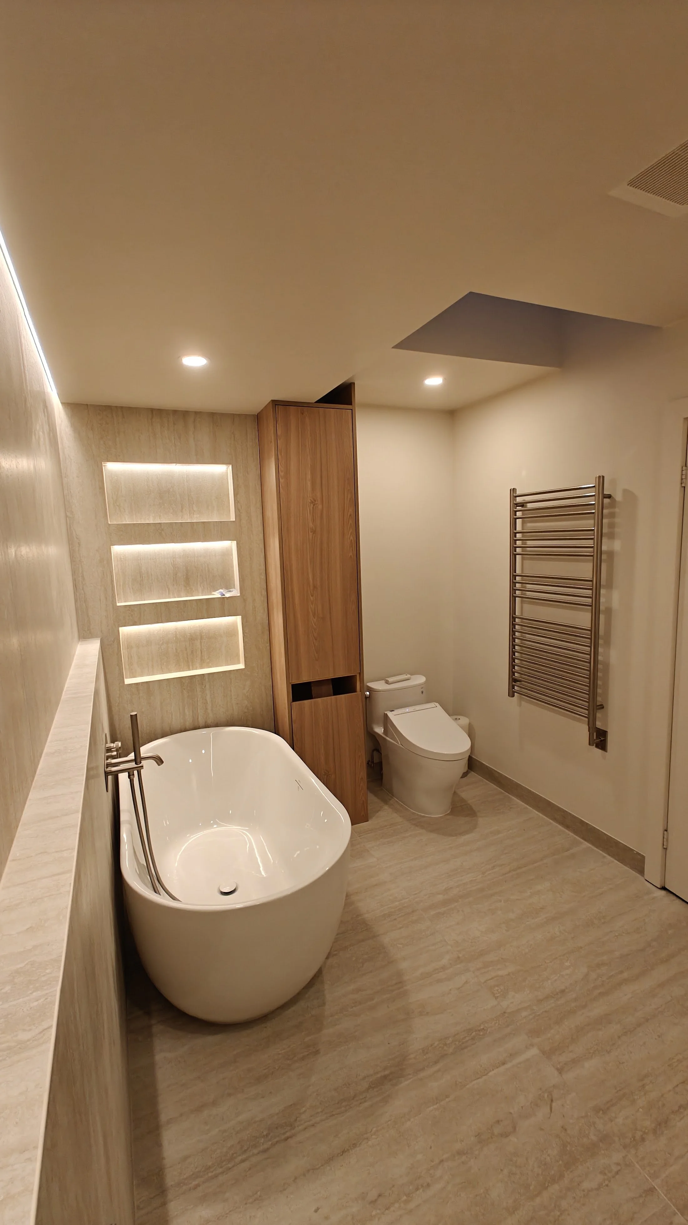 Modern bathroom with a white bathtub, a toilet with a bidet feature, wooden accents, a wall-mounted towel warmer, and recessed lighting.