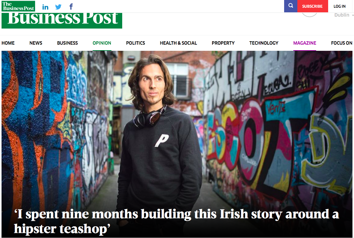 Dylan Townsend article in The Business Post, standing in front of colorful graffiti art on a wall, wearing a black sweatshirt with a white 'P' on it, and headphones around his neck, in an urban alleyway.