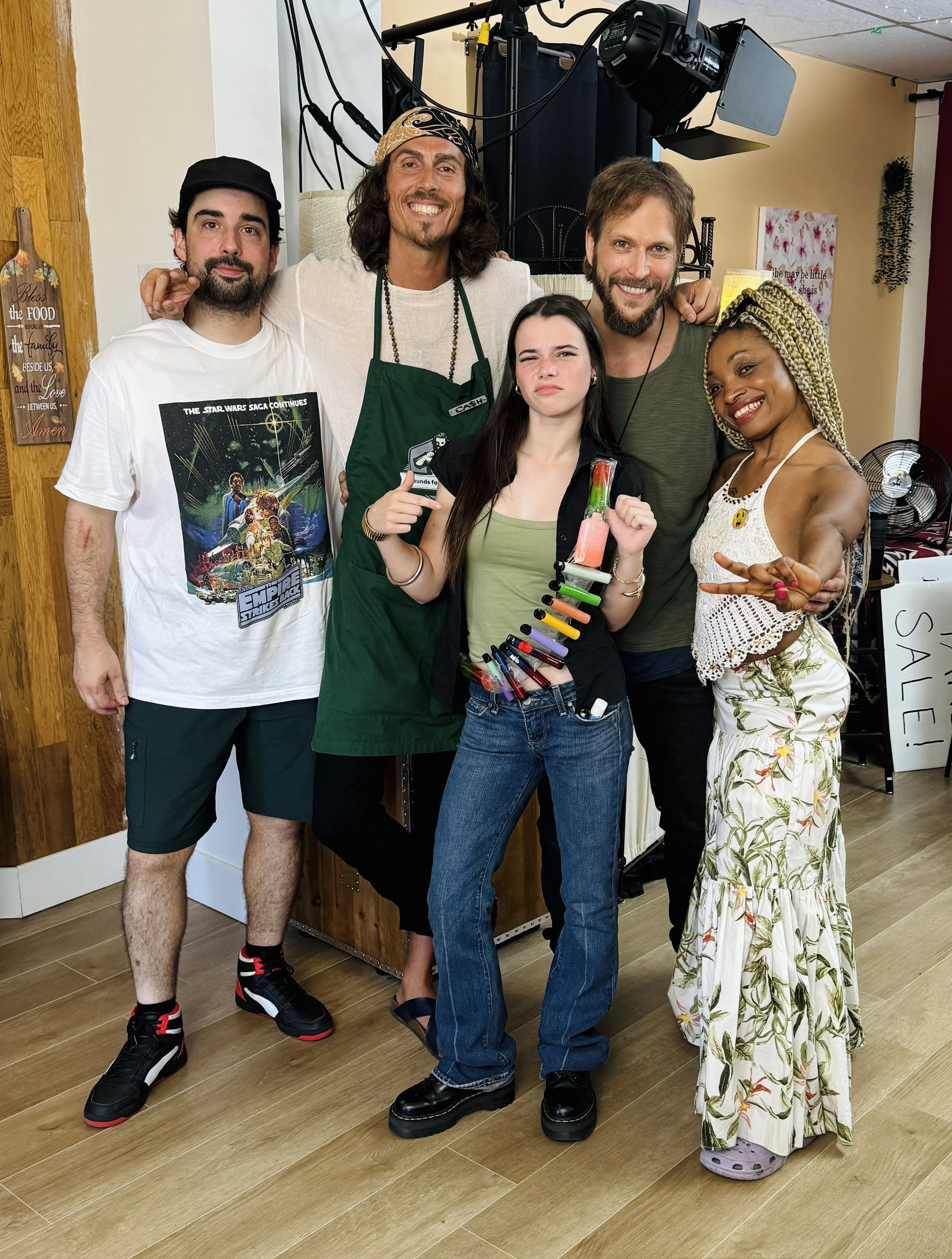 Dylan Townsend on set with people smiling and posing for a photo indoors, standing on wooden floor with some equipment and decor in background.