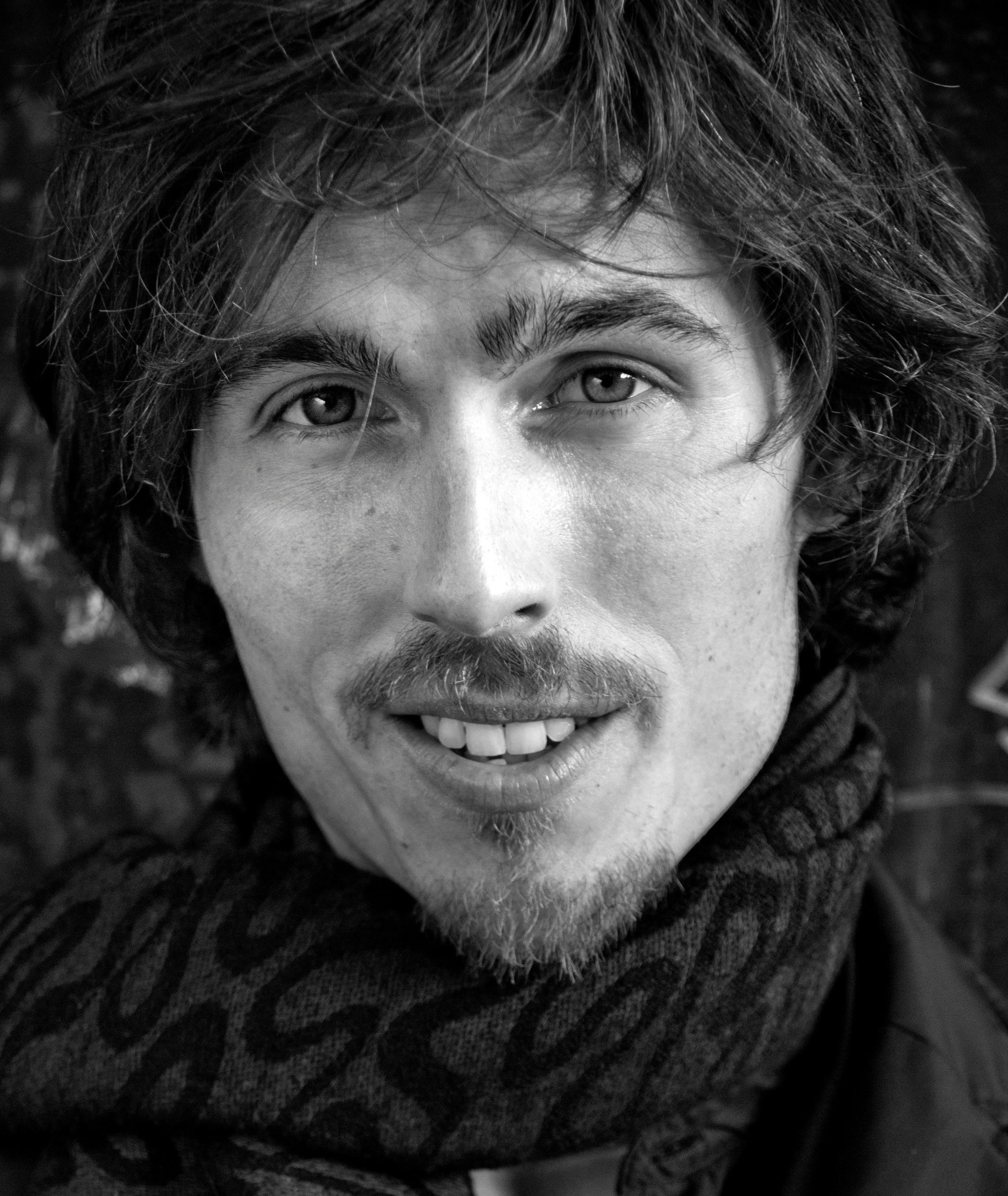 Dylan Townsend Close-up in black and white, showing their eyes, nose, and mouth with curly hair and a beard, smiling.