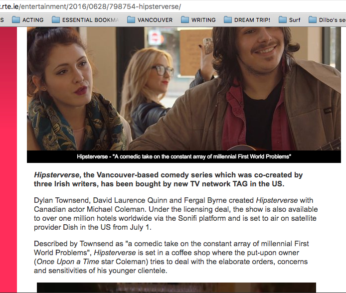 Three people sitting in a coffee shop, two women and a man, with the woman in the background wearing glasses and the man smiling. The woman in the foreground has dark hair and is looking to the side. Article on Hipsterverse, Dylan Townsend.