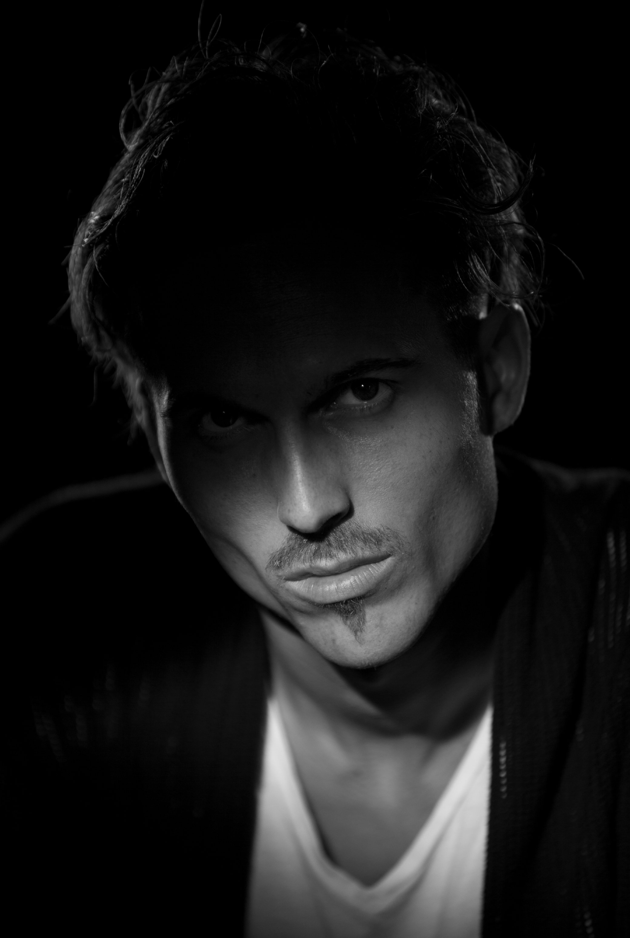 Dylan Townsend. Black and white close-up portrait of a young man with curly hair, showing intense eyes and part of his nose and lips, wearing a white shirt and a dark jacket.