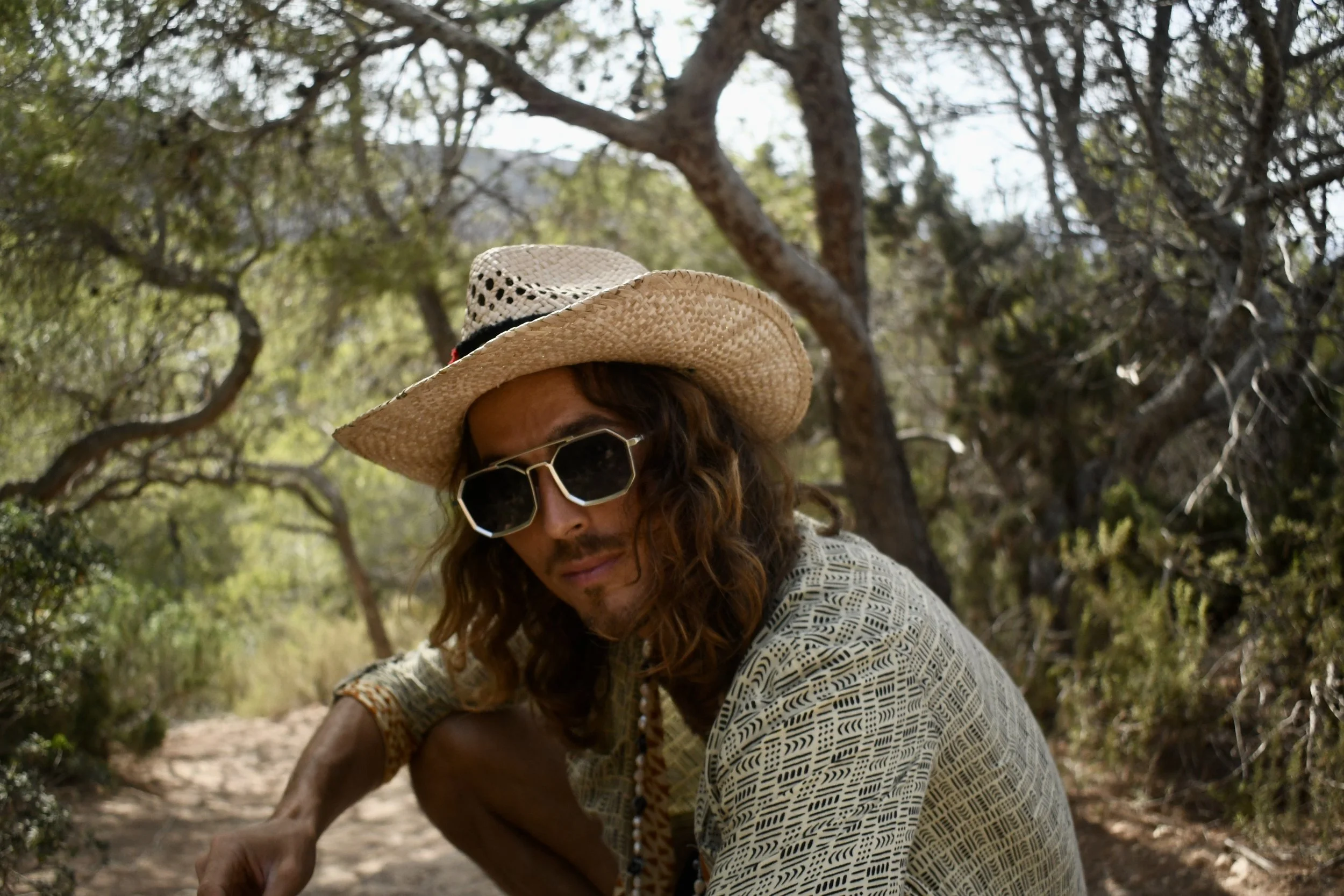 Dylan Townsend wearing straw hat and sunglasses, outdoors in a wooded area in Ibiza.