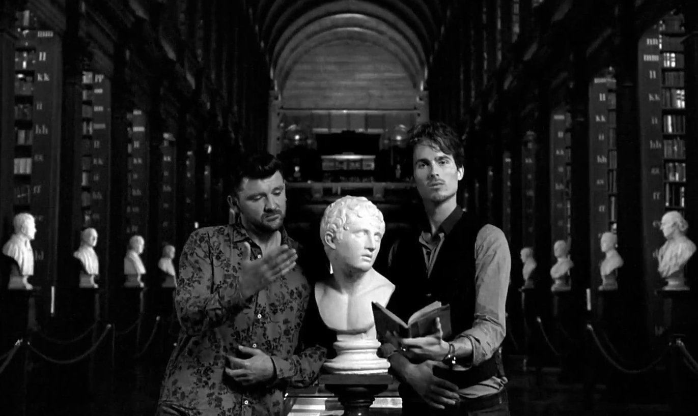 Dylan Townsend Guinness commercial in Trinity library. The library has tall wooden shelves filled with books and classical busts along the aisle.