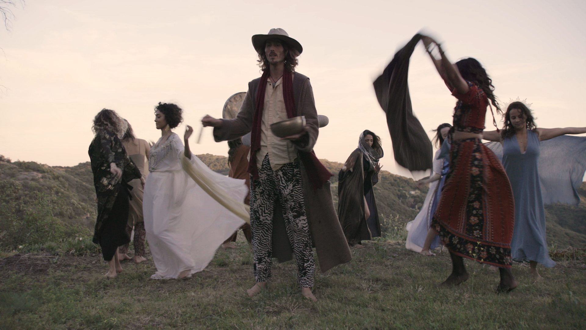 Dylan Townsend still from Tv Pilot 'Intentional' A group of diverse people in bohemian clothing dancing outdoors on a grassy hill at sunset. Topanga Canyon.