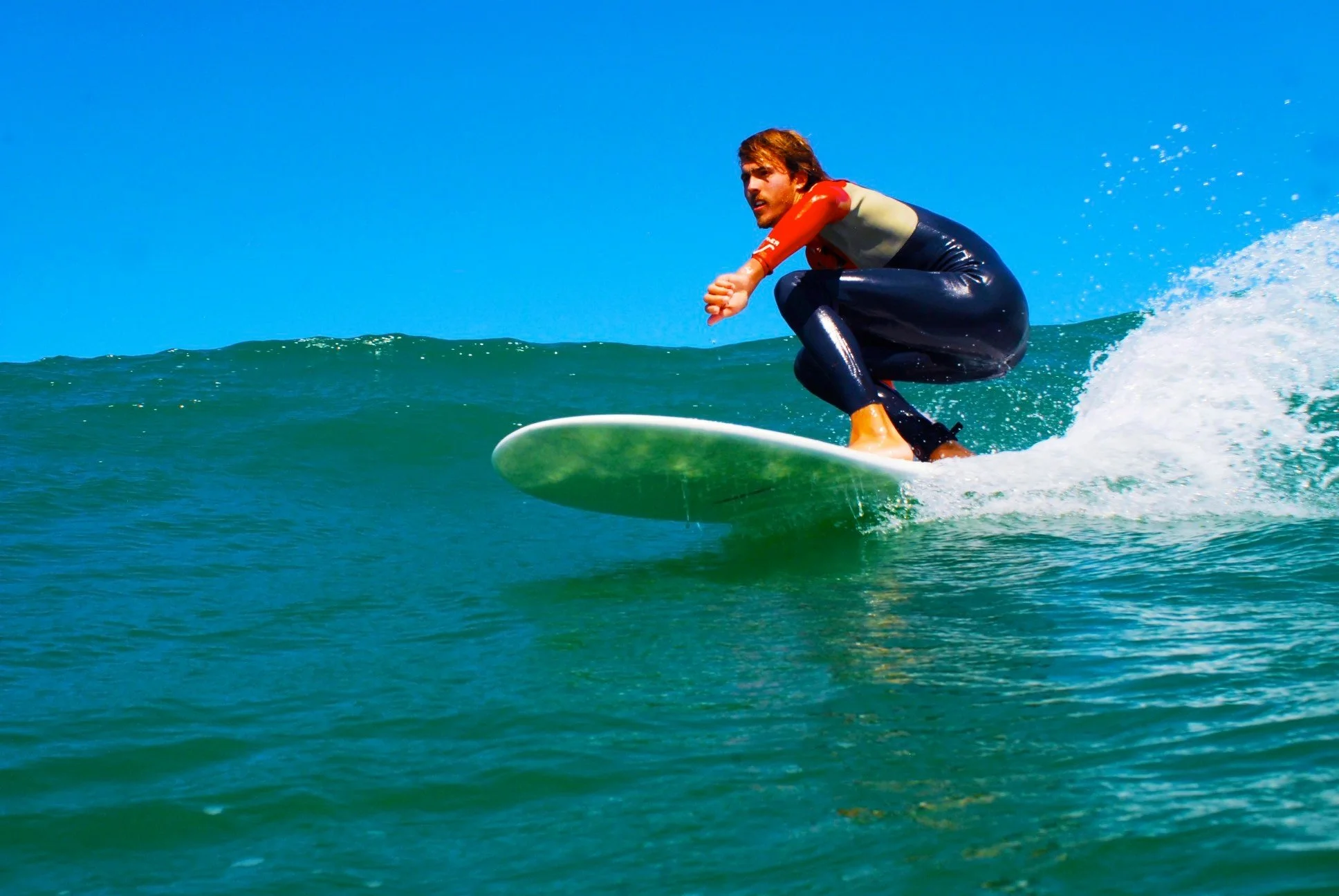 Dylan Townsend. Male surfer riding a wave on a surfboard in the ocean under a clear blue sky.