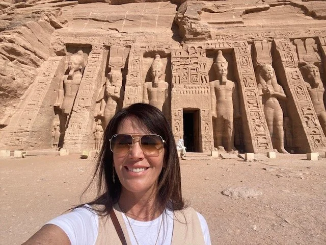 Julie Ann Beijer  taking a selfie in front of the ancient Abu Simbel temples in Egypt, with large statues and hieroglyphics carved into the rock face behind her.