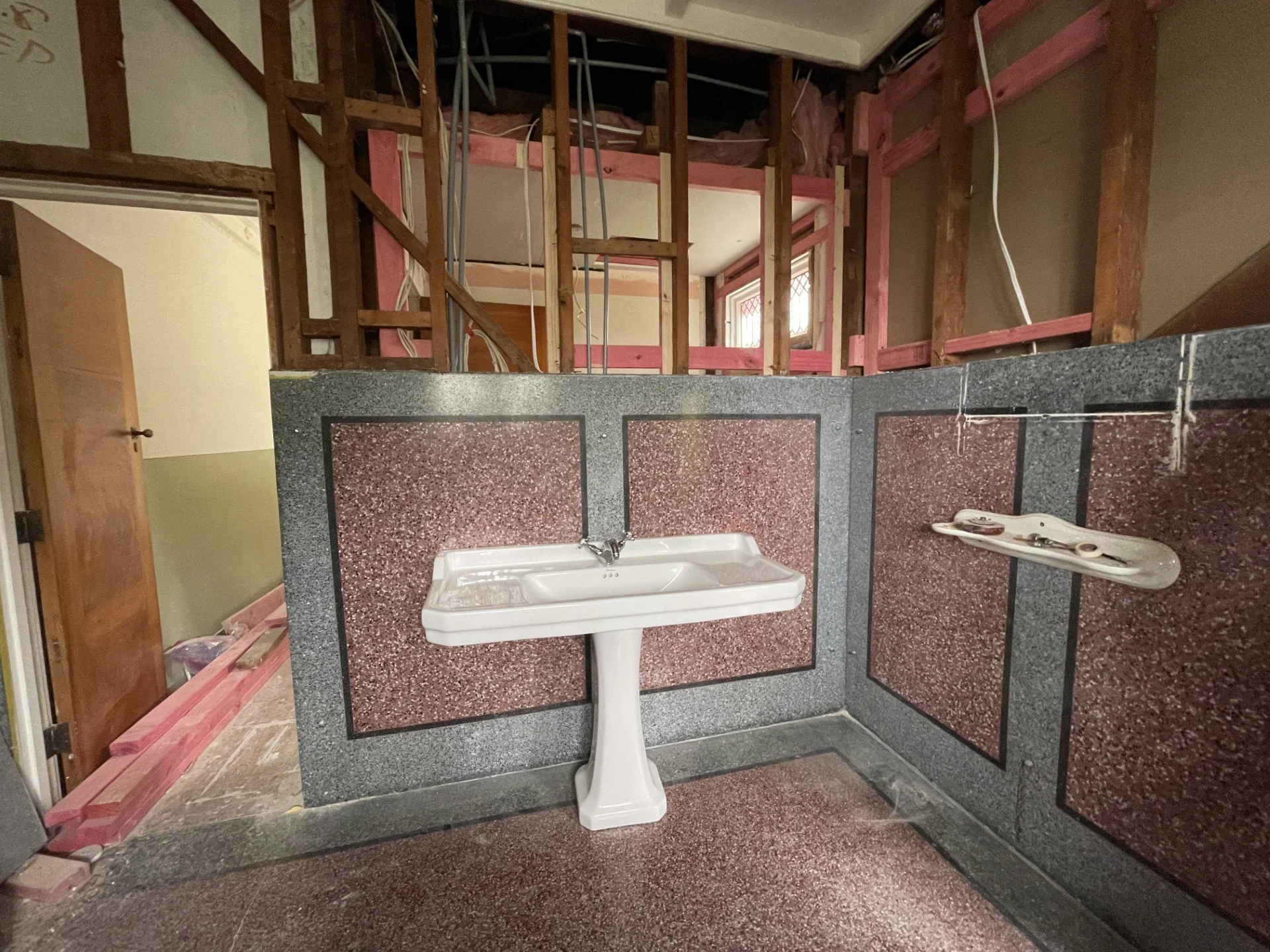 Bathroom under renovation with exposed wooden framing, a granite countertop with a sink, and construction supplies.