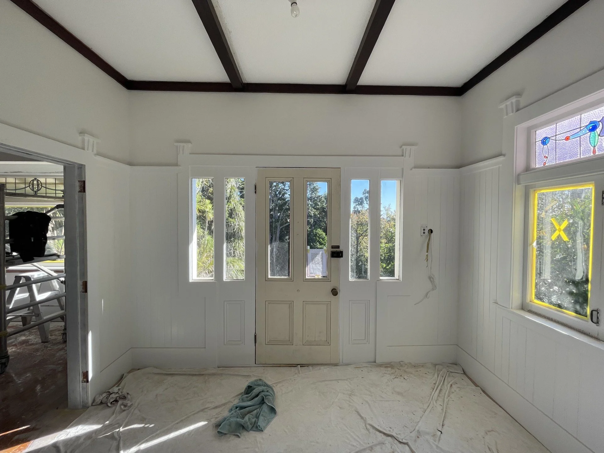 Interior of a house under construction with white walls and door, tools, and construction materials visible.