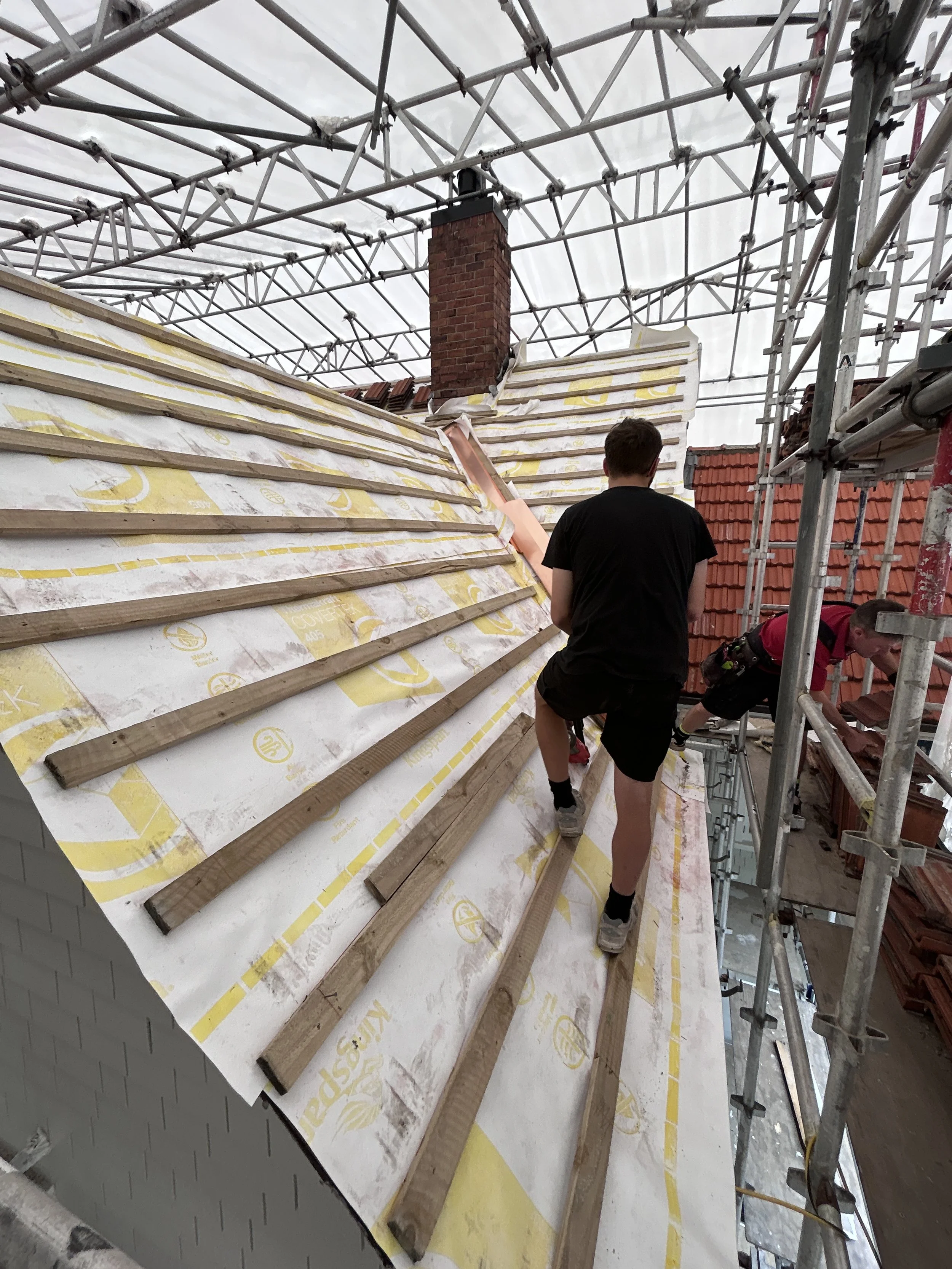 Construction workers installing roofing on a house, with scaffolding and insulation material on the roof.