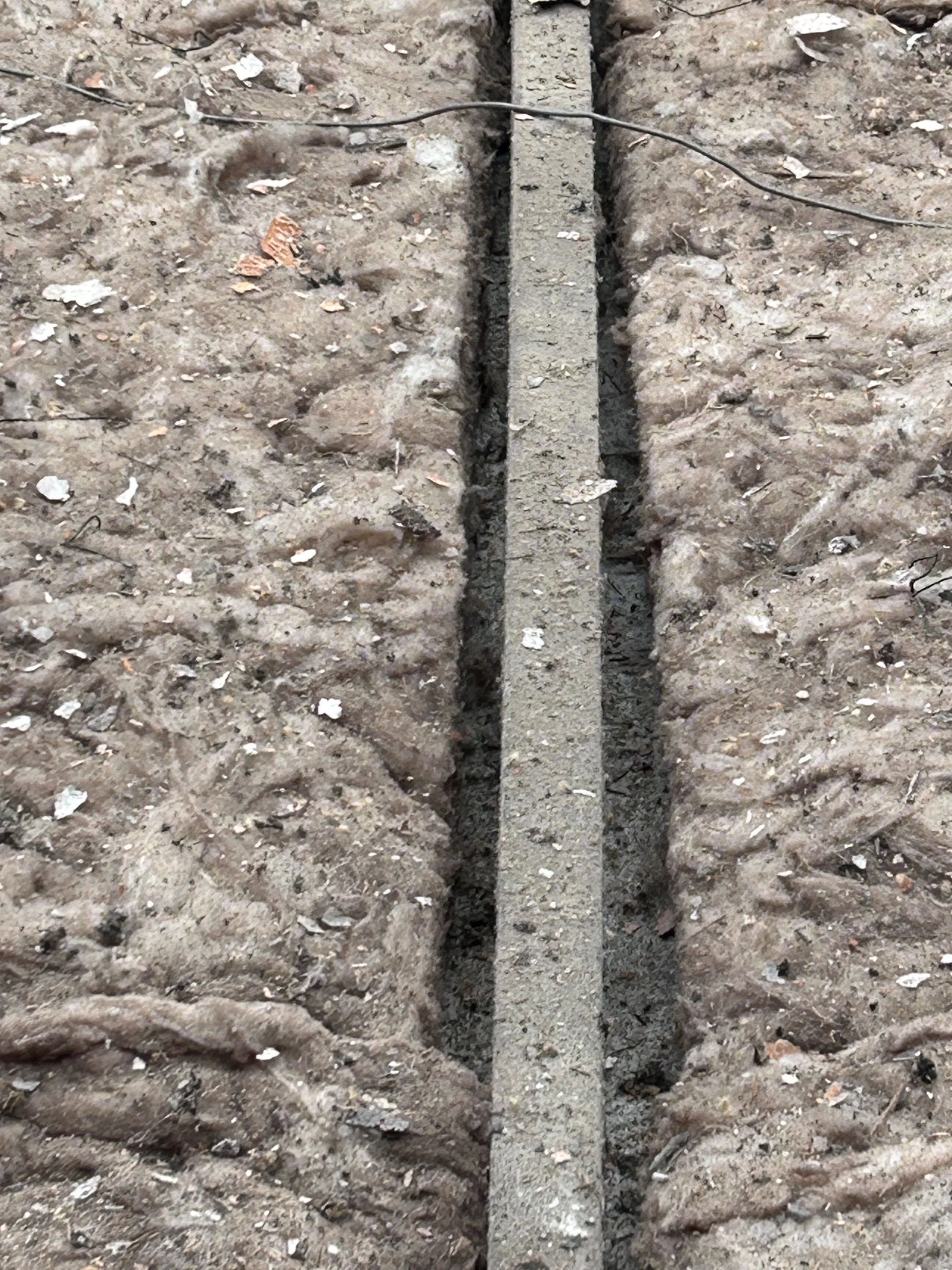 A partially dug trench with a concrete block in the middle, surrounded by excavated soil and debris.