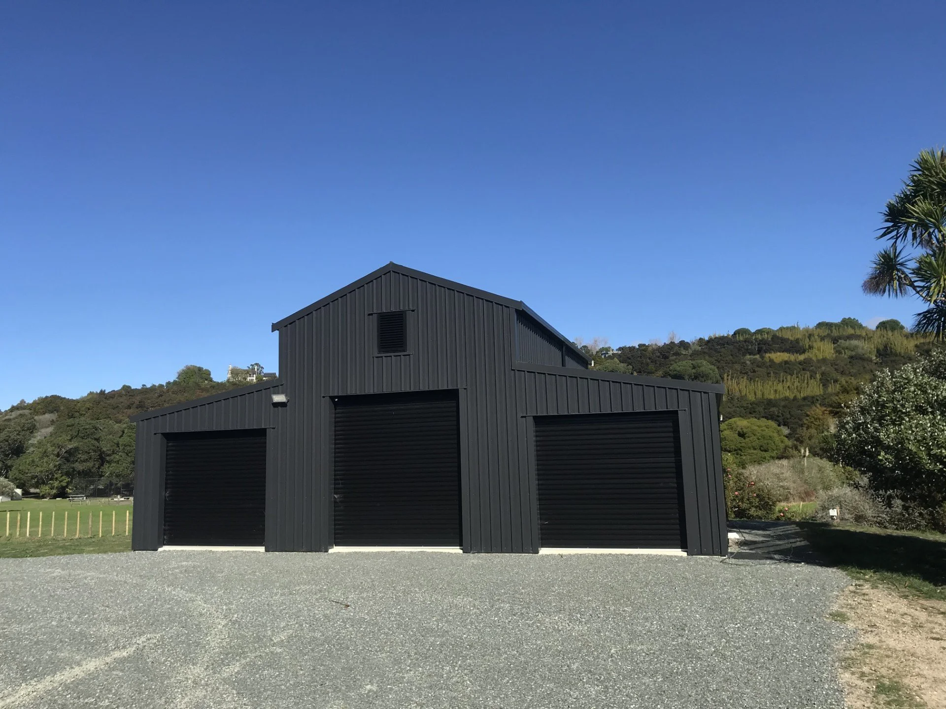 A black metal building with large garage doors, set against a backdrop of green hills and a clear blue sky.