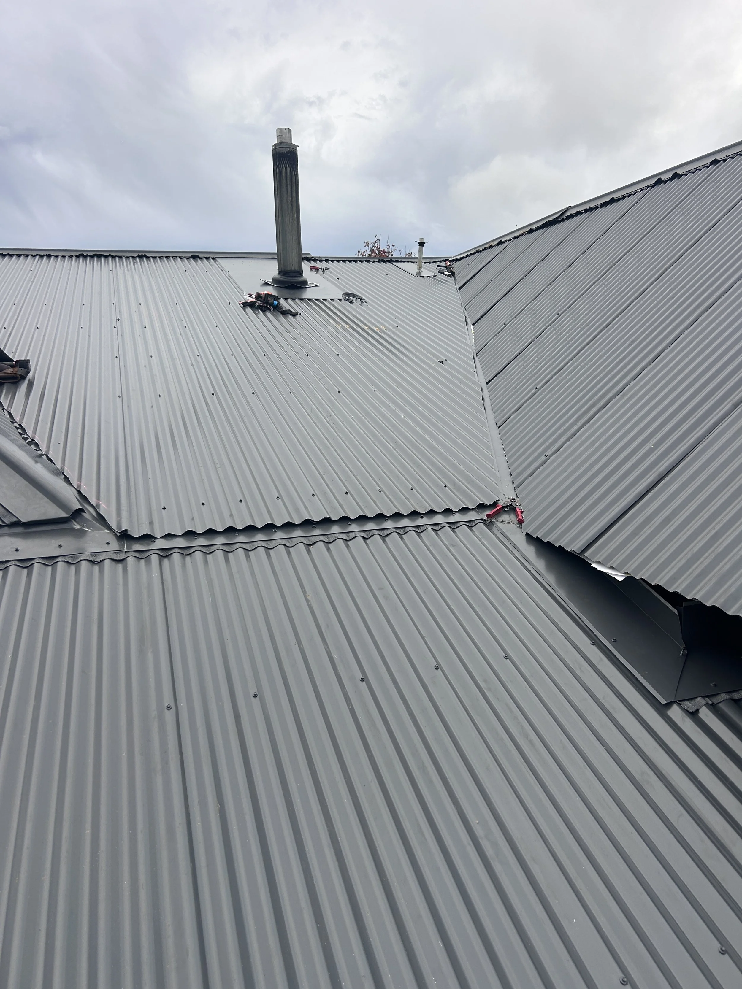 Metal roof with two ventilation pipes, one taller than the other, and part of a cloudy sky in the background.