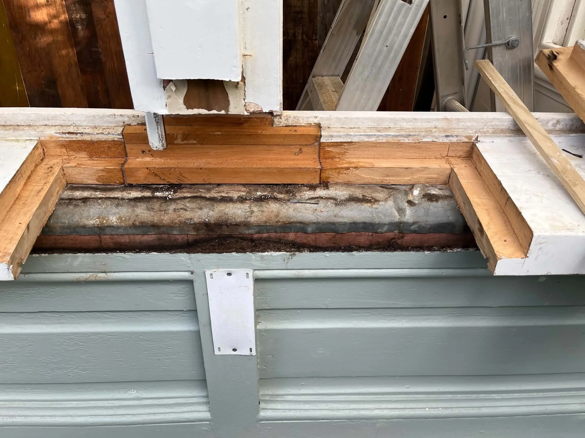 Close-up of a house wall with exposed framing and installed siding, showing a section of siding removed with tools and wood visible.