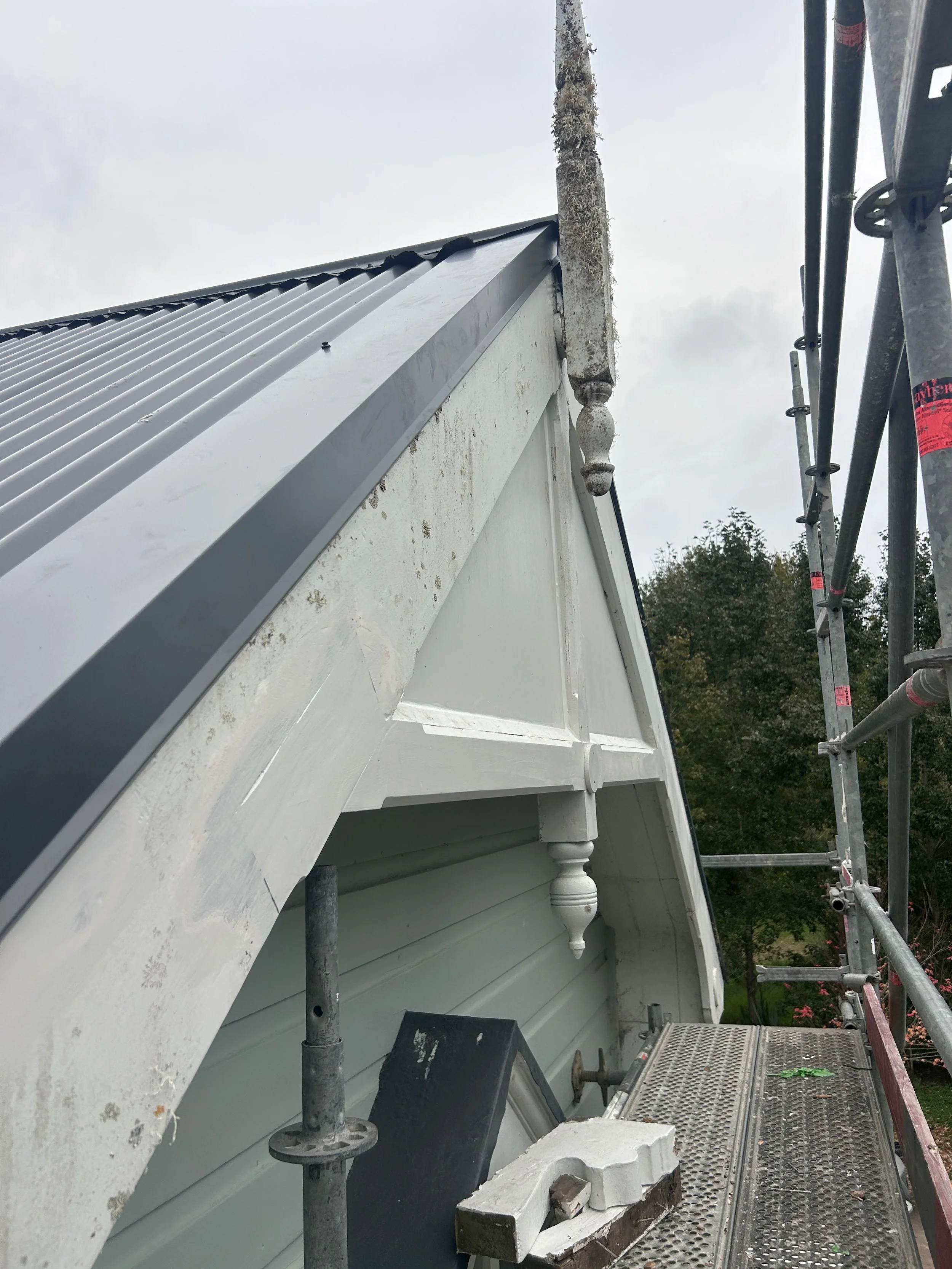The image shows an exterior corner of a white building where white exterior paint is being applied, with scaffolding on the side for construction or renovation work.