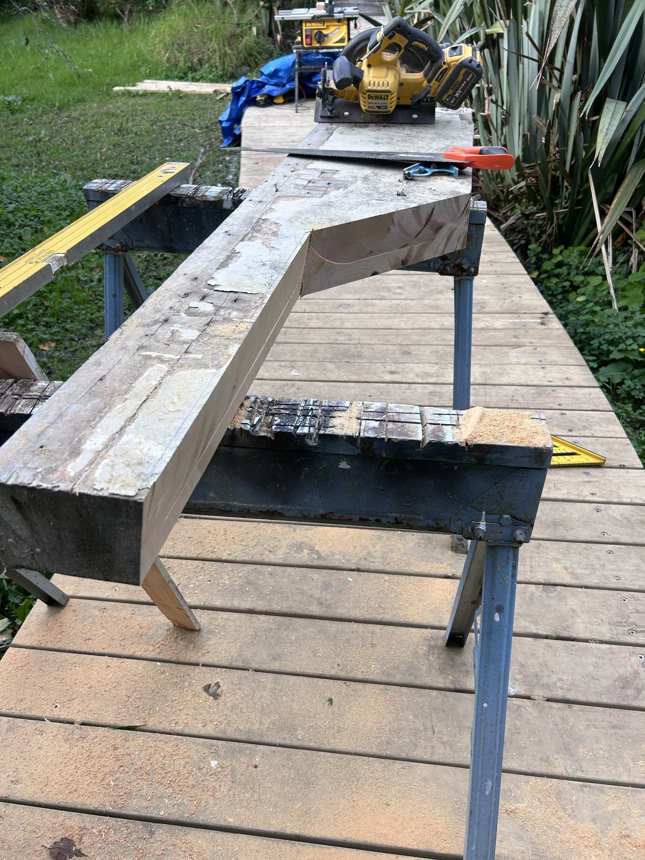 A workbench outdoors with a circular saw, a level, and clamps. Wooden planks and tools are arranged for a woodworking project.
