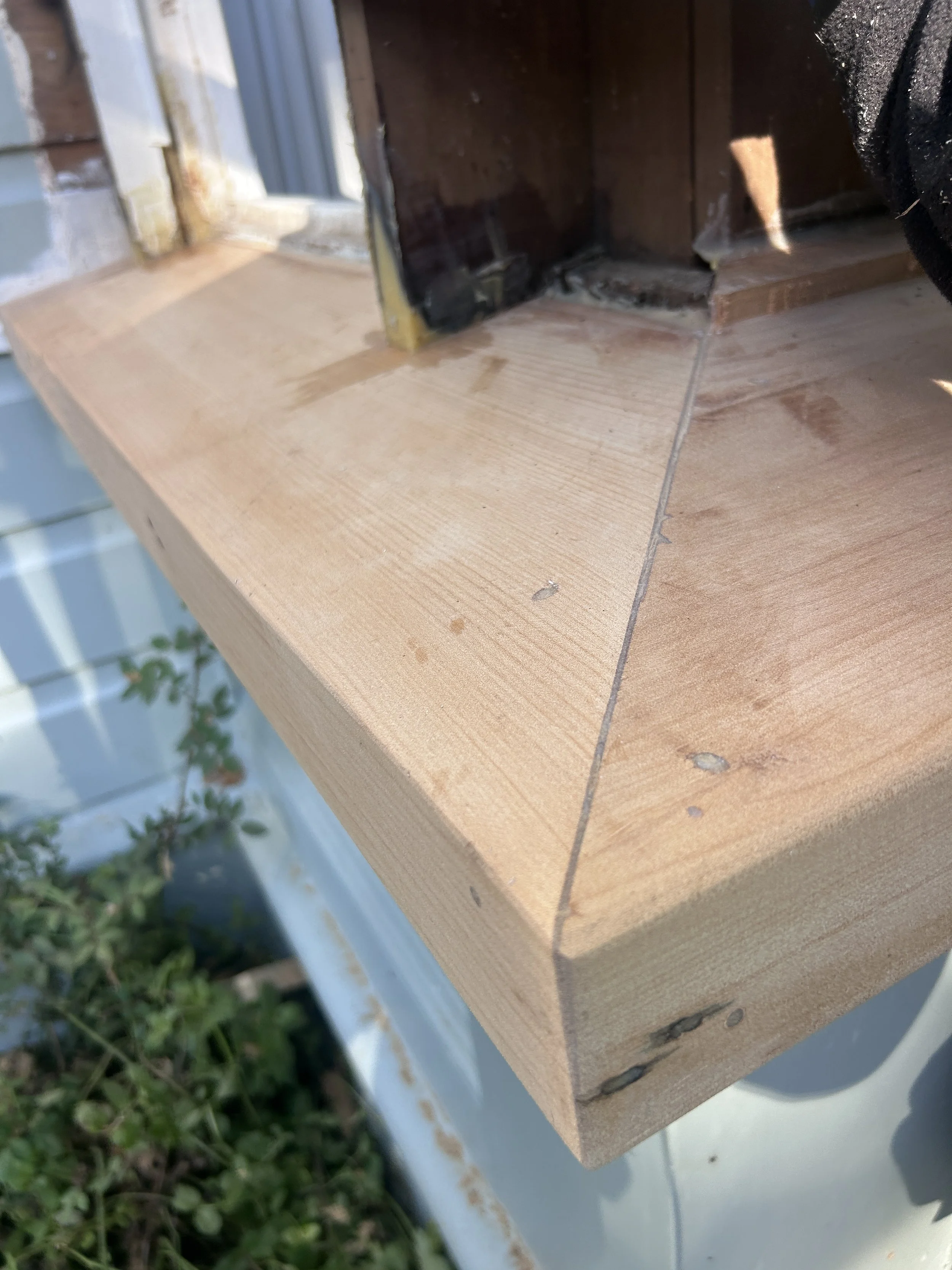 Close-up image of a wooden structure, possibly a piece of furniture or a part of a construction project, with visible screws and joints, outdoors near grass and a light-colored surface.