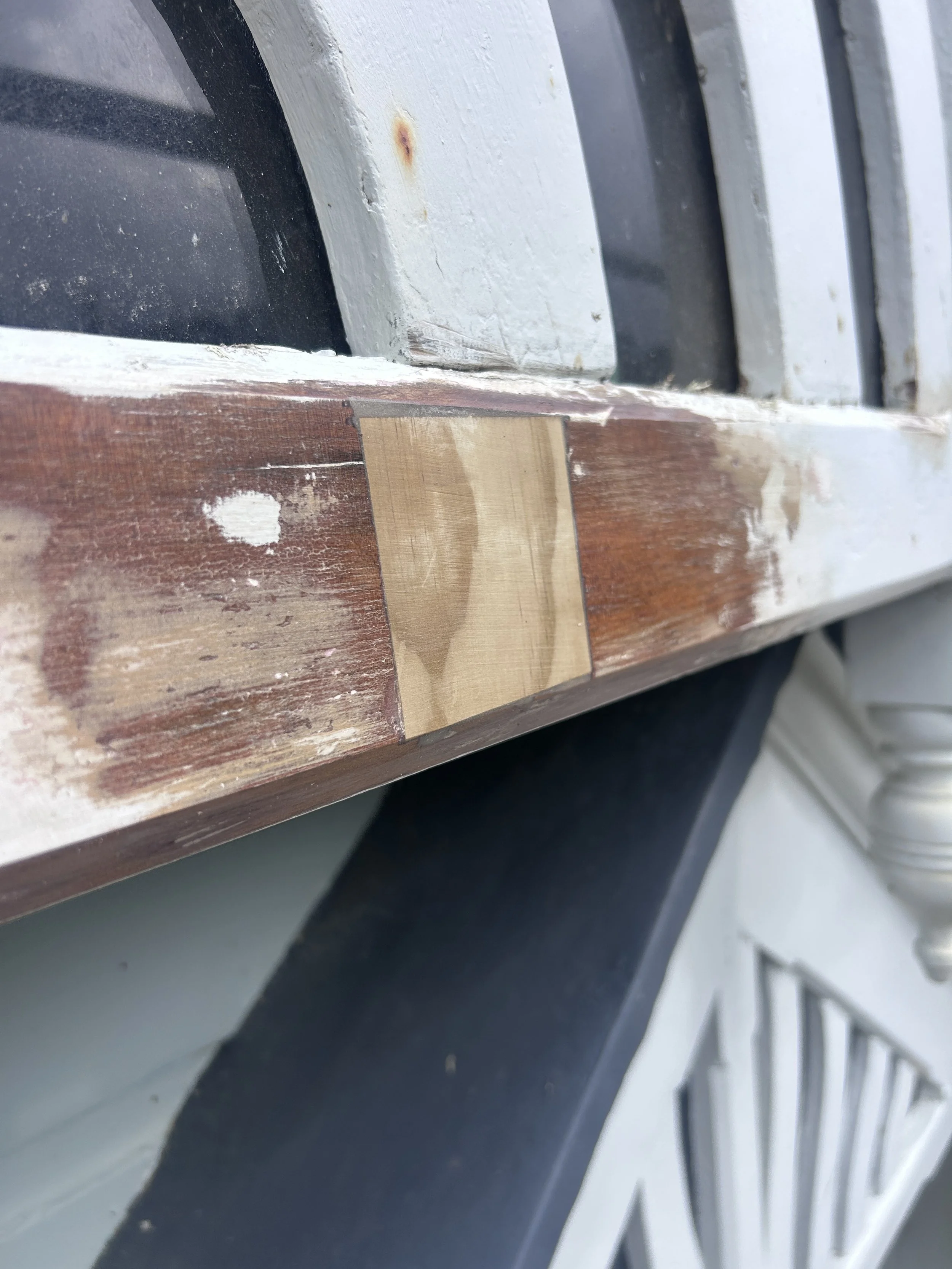 Close-up of a wooden surface with a piece of tape and some paint, next to a white painted surface with a rusty spot. The focus is on the edge where the two surfaces meet.