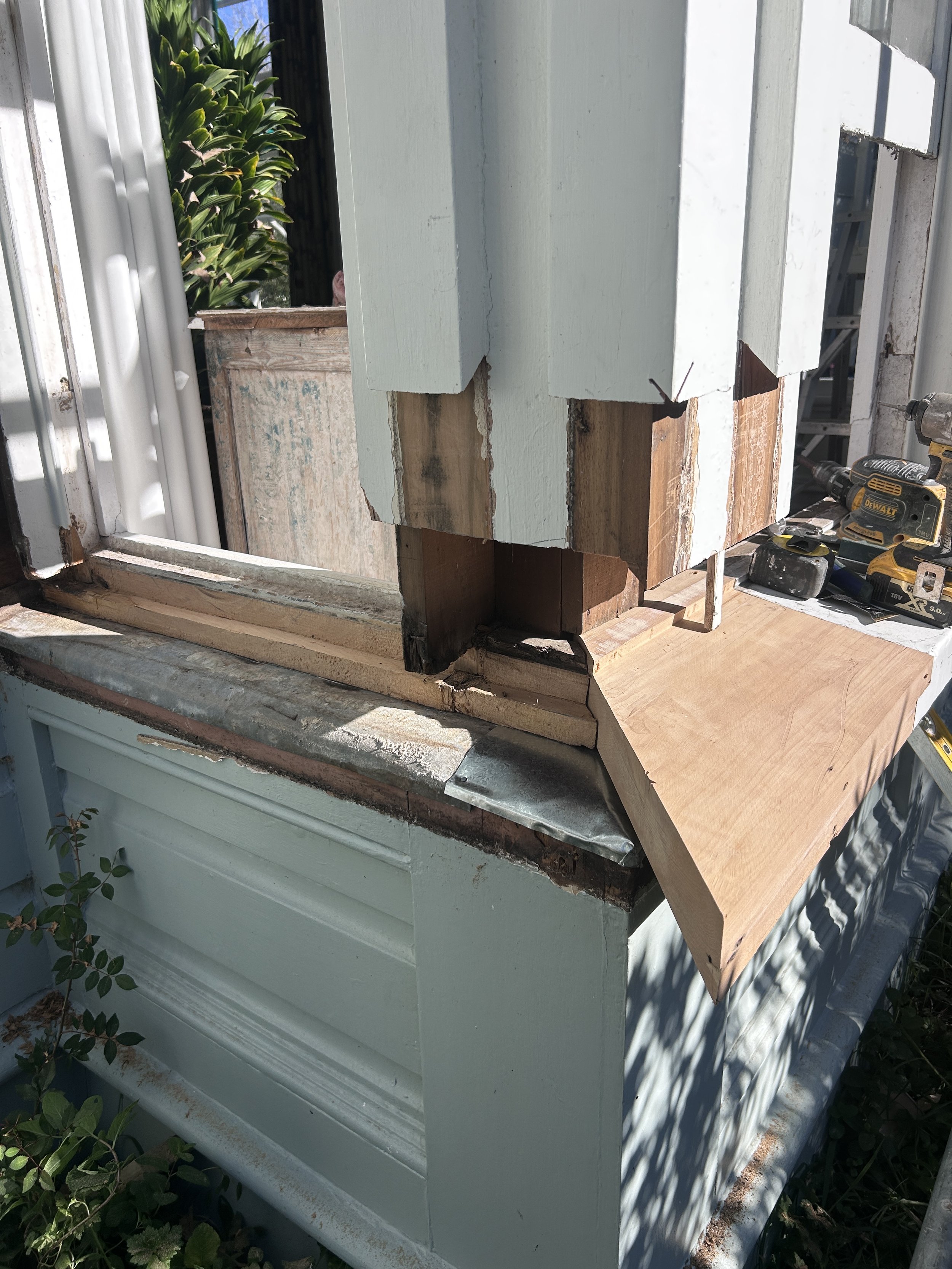 Close-up of a partially reconstructed window frame with green painted siding and visible wooden framework, construction tools visible to the right.